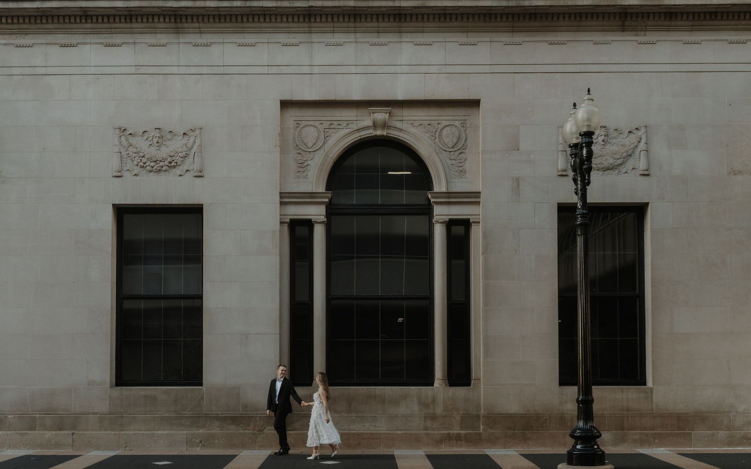 A couple standing outside an elegant stone building with arched entrance and ornate architectural details.