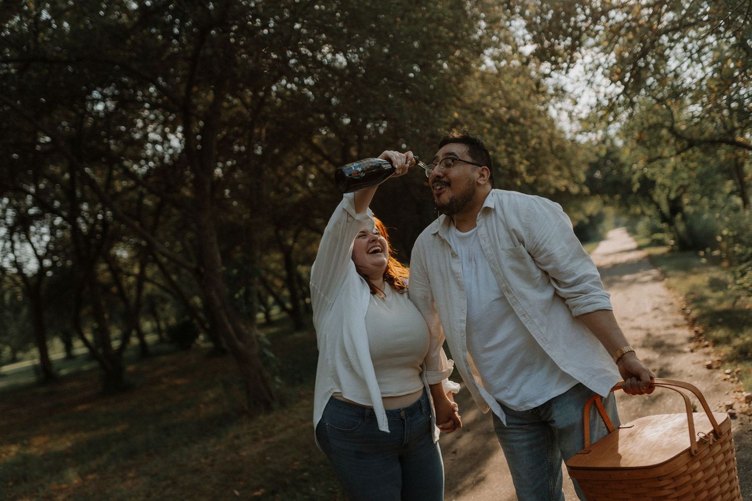 A couple shares an intimate outdoor moment at sunset in a rustic park setting with golden sunlight filtering through trees.