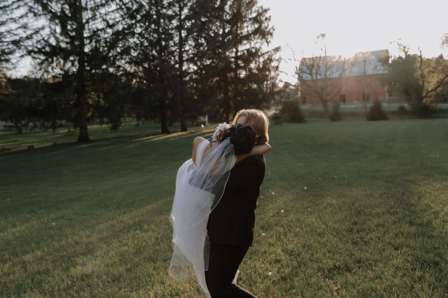 A couple embraces in golden sunlight on a grassy hillside during sunset.
