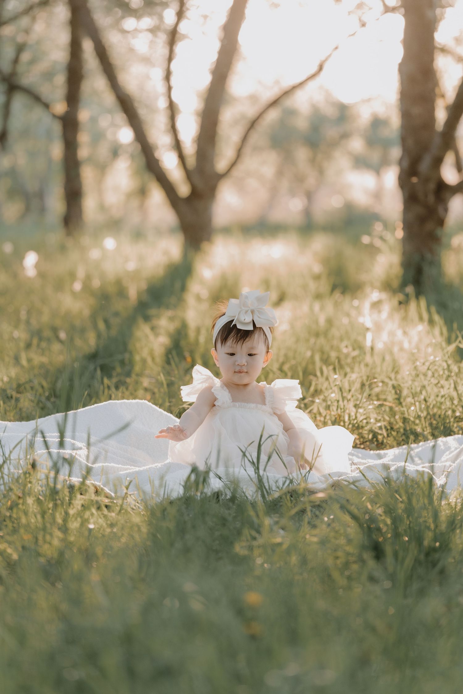 A child wearing white lies in tall grass during a dreamy outdoor photoshoot in soft sunlight.