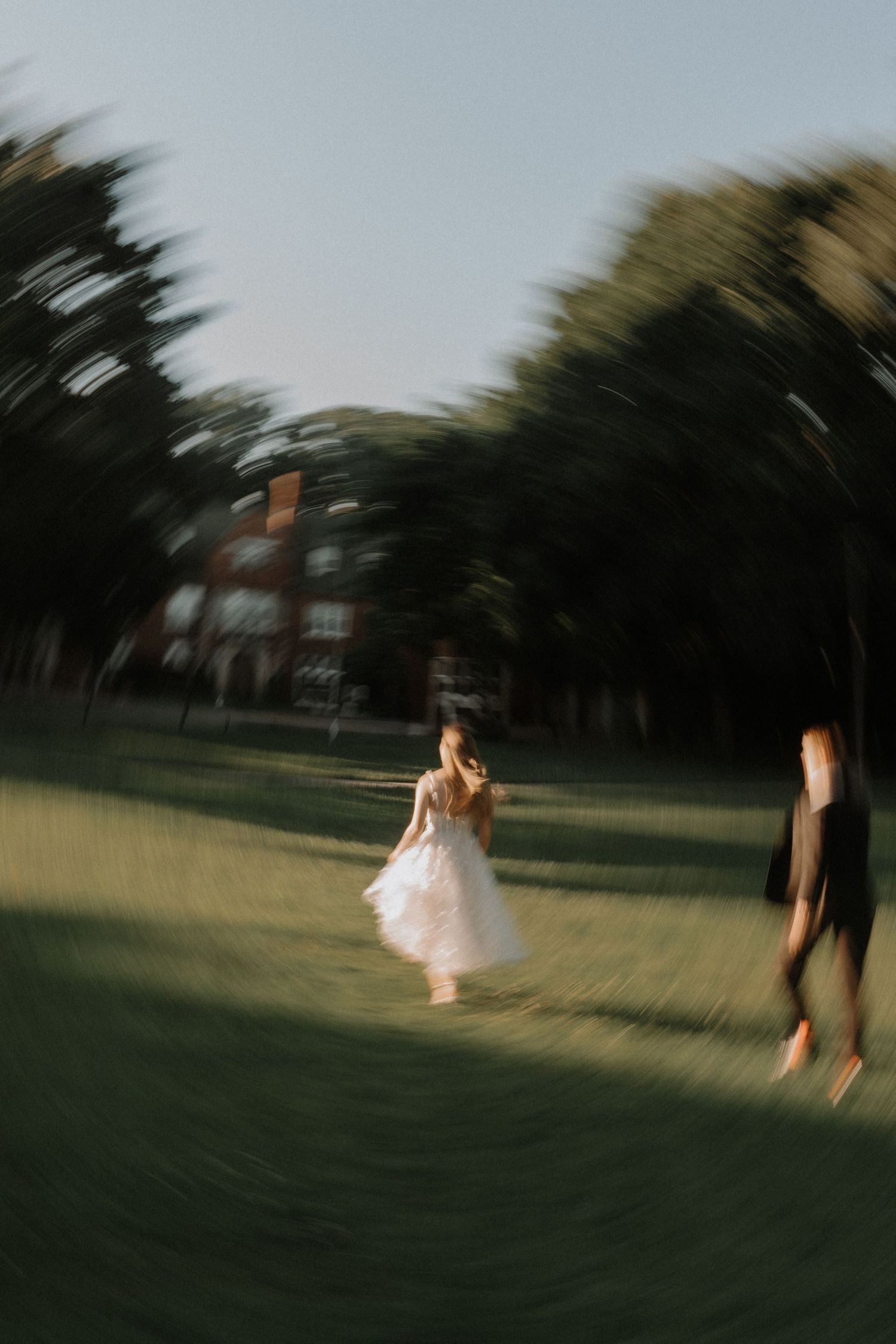 Motion blur captures a couple in formal attire running across a grassy field at twilight.
