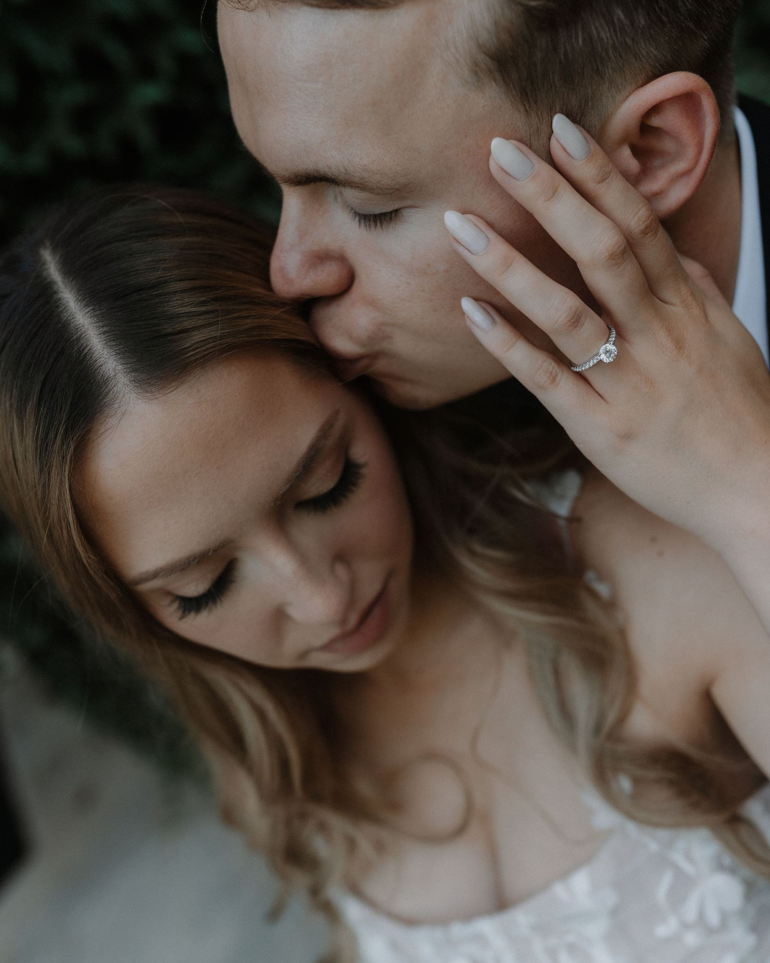 Intimate wedding photography captures embrace in moody lighting with delicate lace dress details.