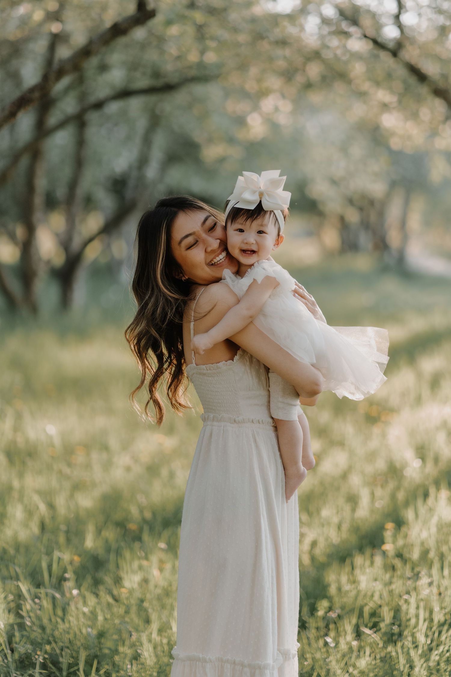 A joyful moment captured in a sunlit field as mother and baby share laughter while wearing matching white dresses.