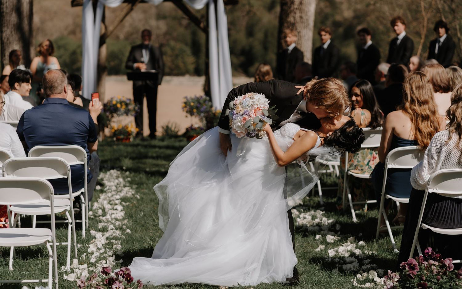 White chairs set up for an outdoor garden wedding ceremony under trees.