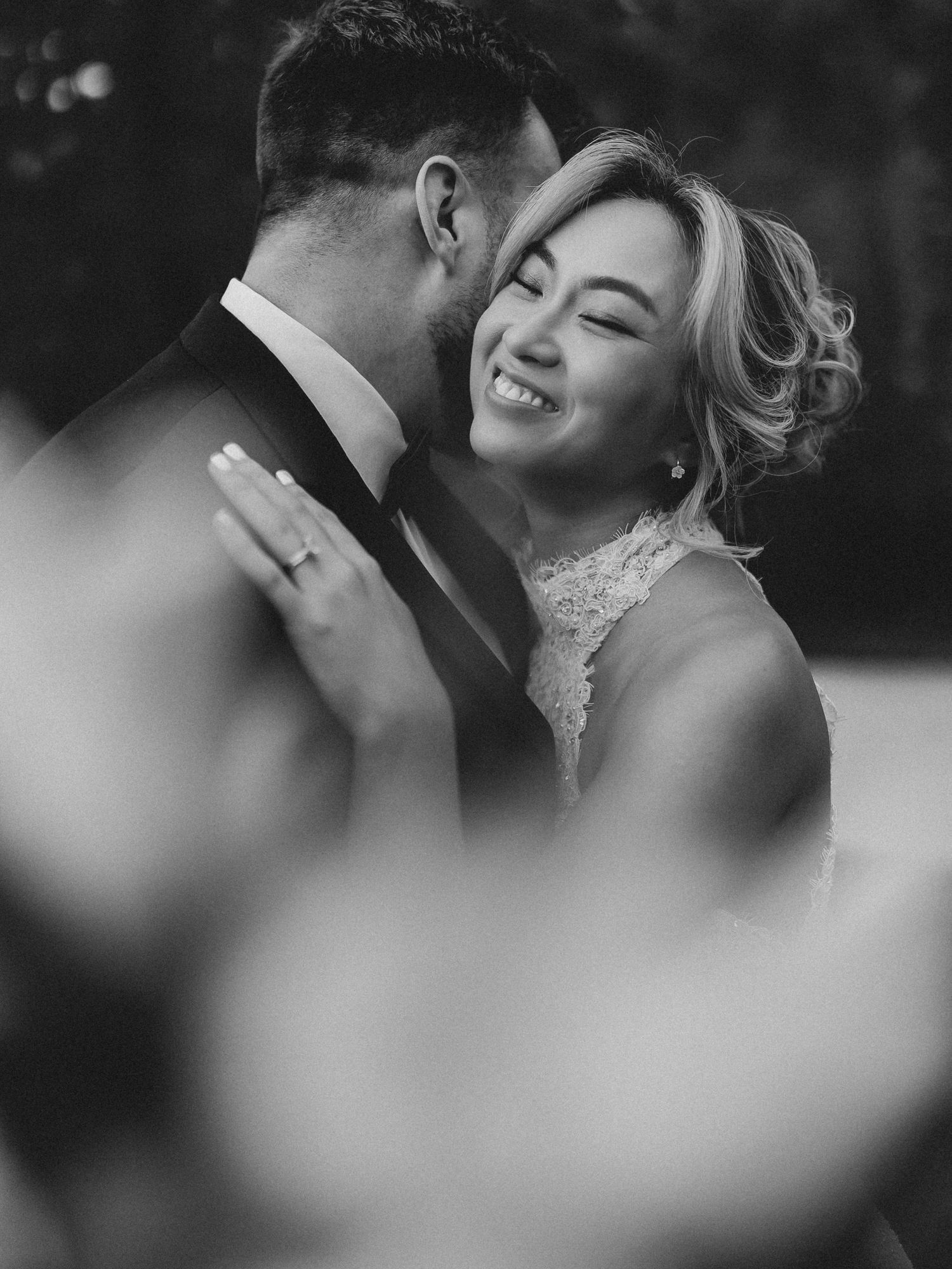 Black and white wedding photo of a smiling bride and groom sharing an intimate moment, bride wearing lace dress.