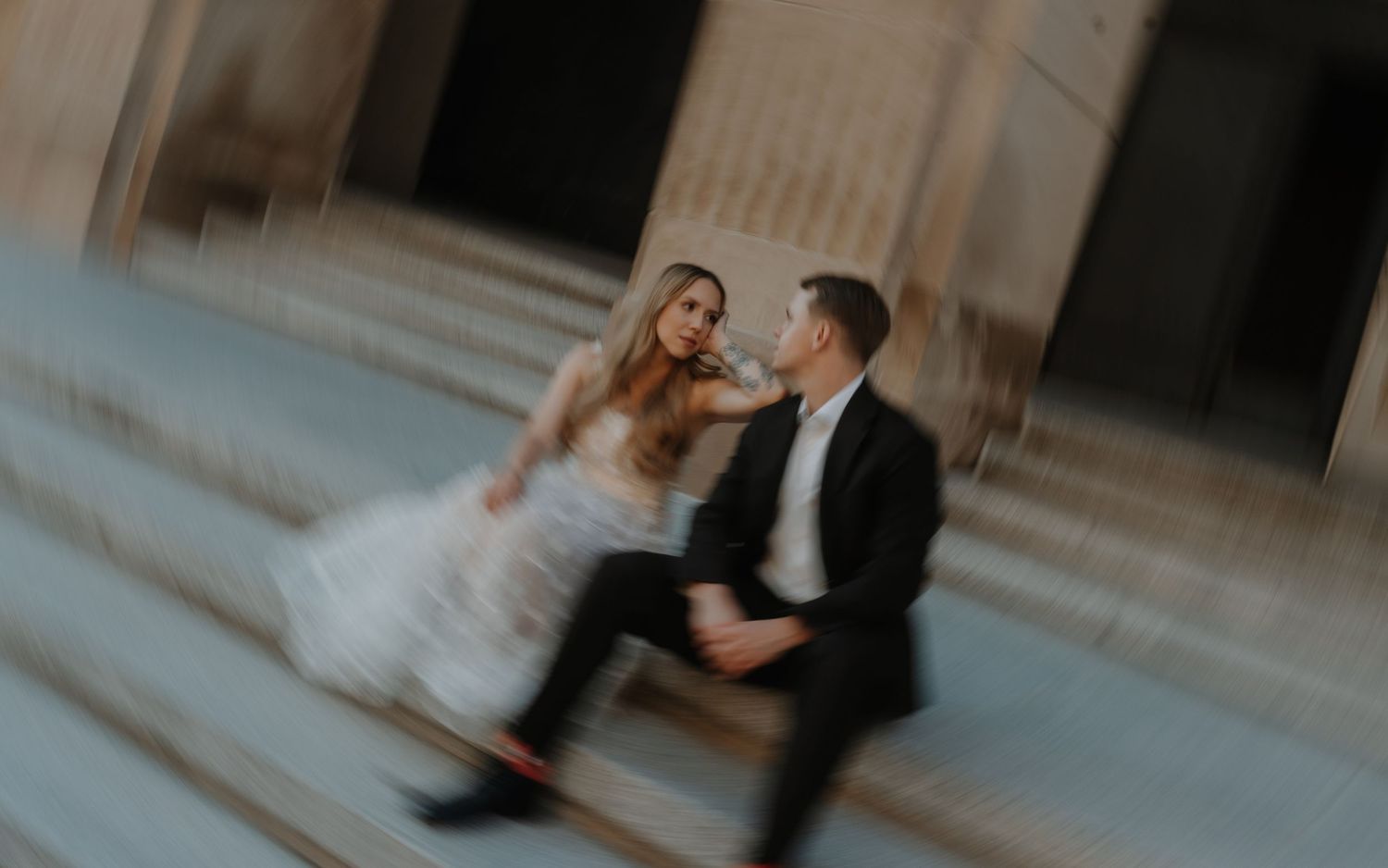 Romantic wedding couple embraces while dancing on marble steps in an elegant venue.