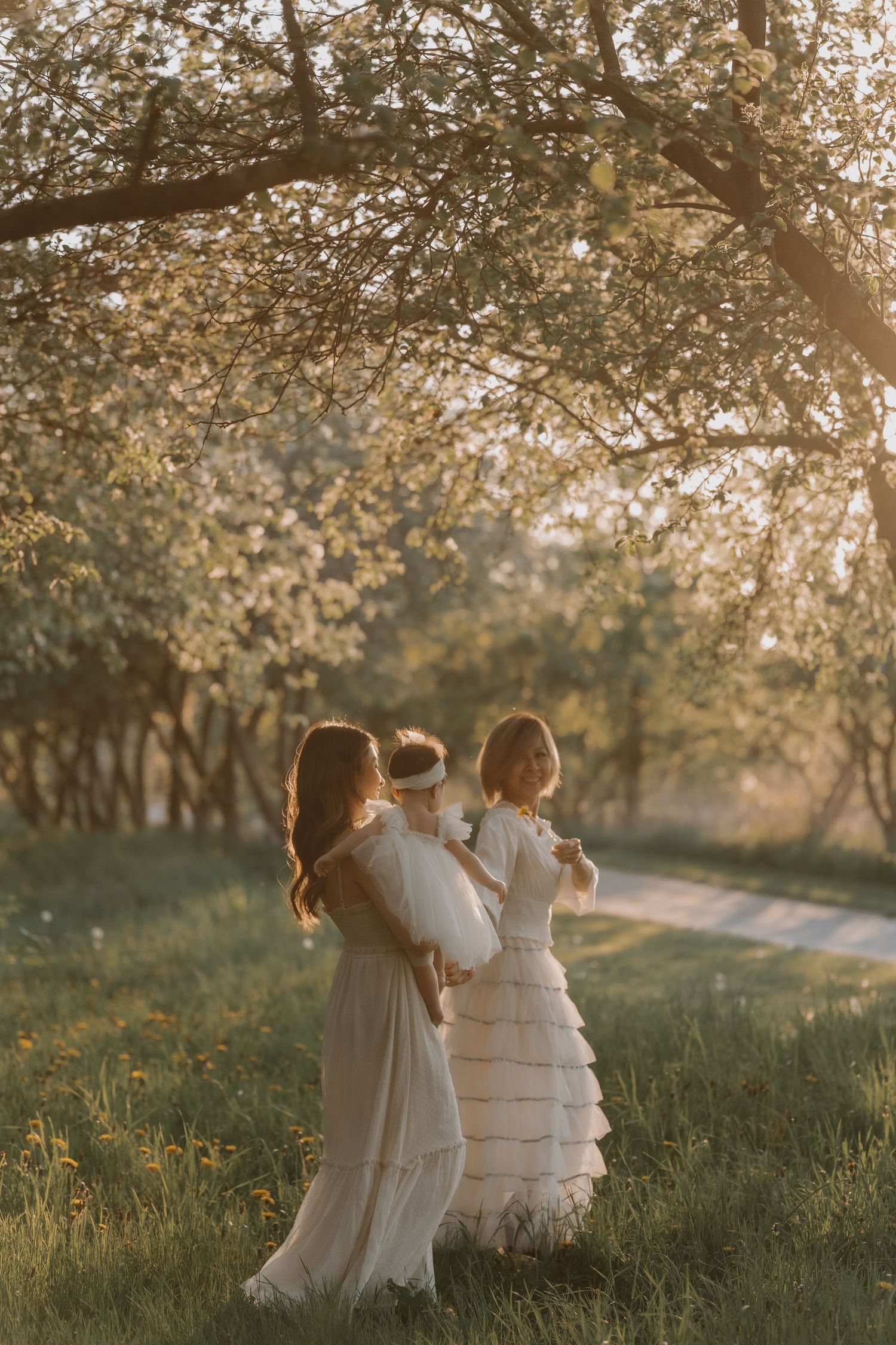 Children in white dresses walking together through a sunlit spring orchard at golden hour.