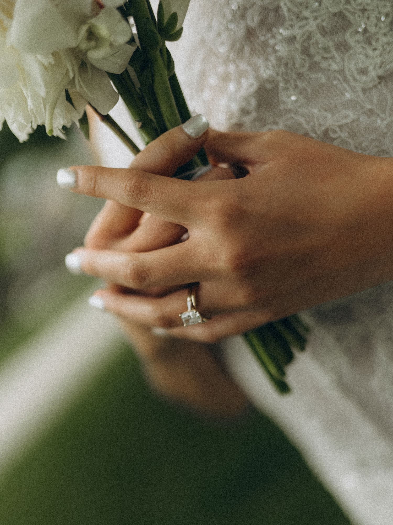 Close-up of a bride holding white flowers, showcasing a stunning diamond solitaire engagement ring on her finger.