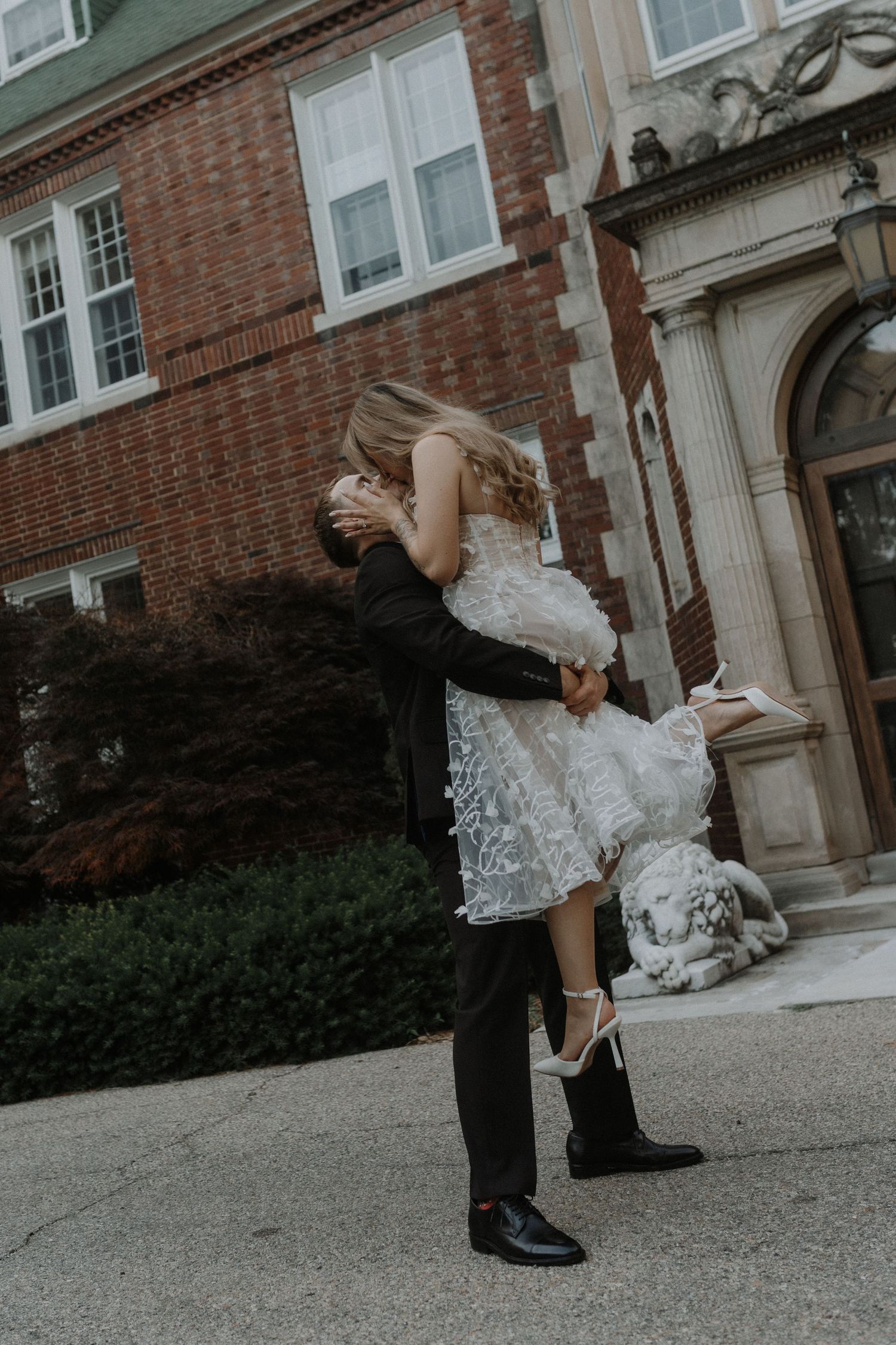 Playful wedding couple dances and spins on the grounds of a historic brick building.