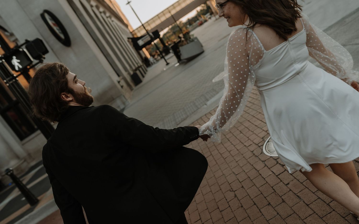 A bride walks through an indoor venue wearing a white lace wedding dress with long sleeves.