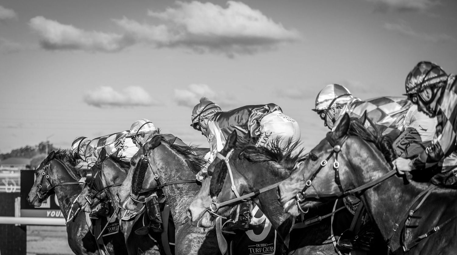 Black and white action shot of horses racing in close formation.