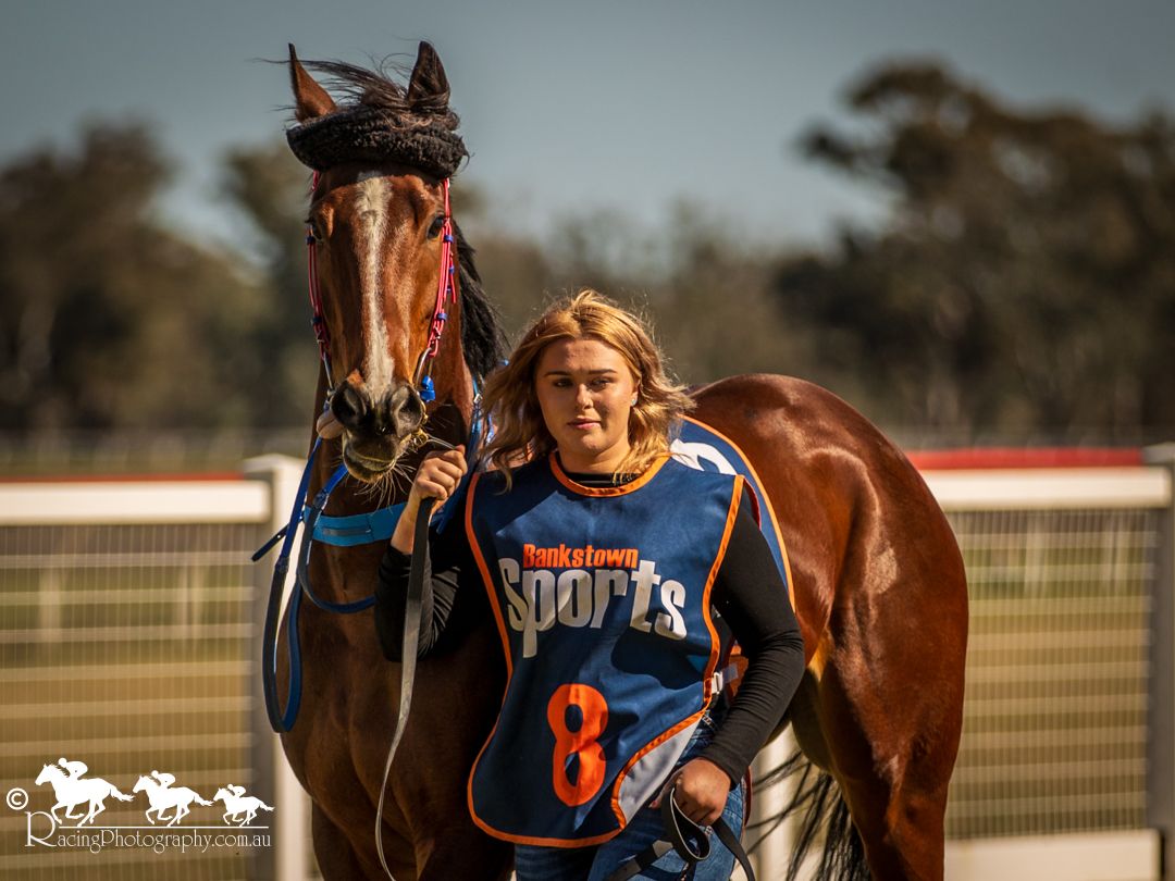 Young jockey in Ducktown Sports jersey number 8 leading a bay horse at a rural racetrack.