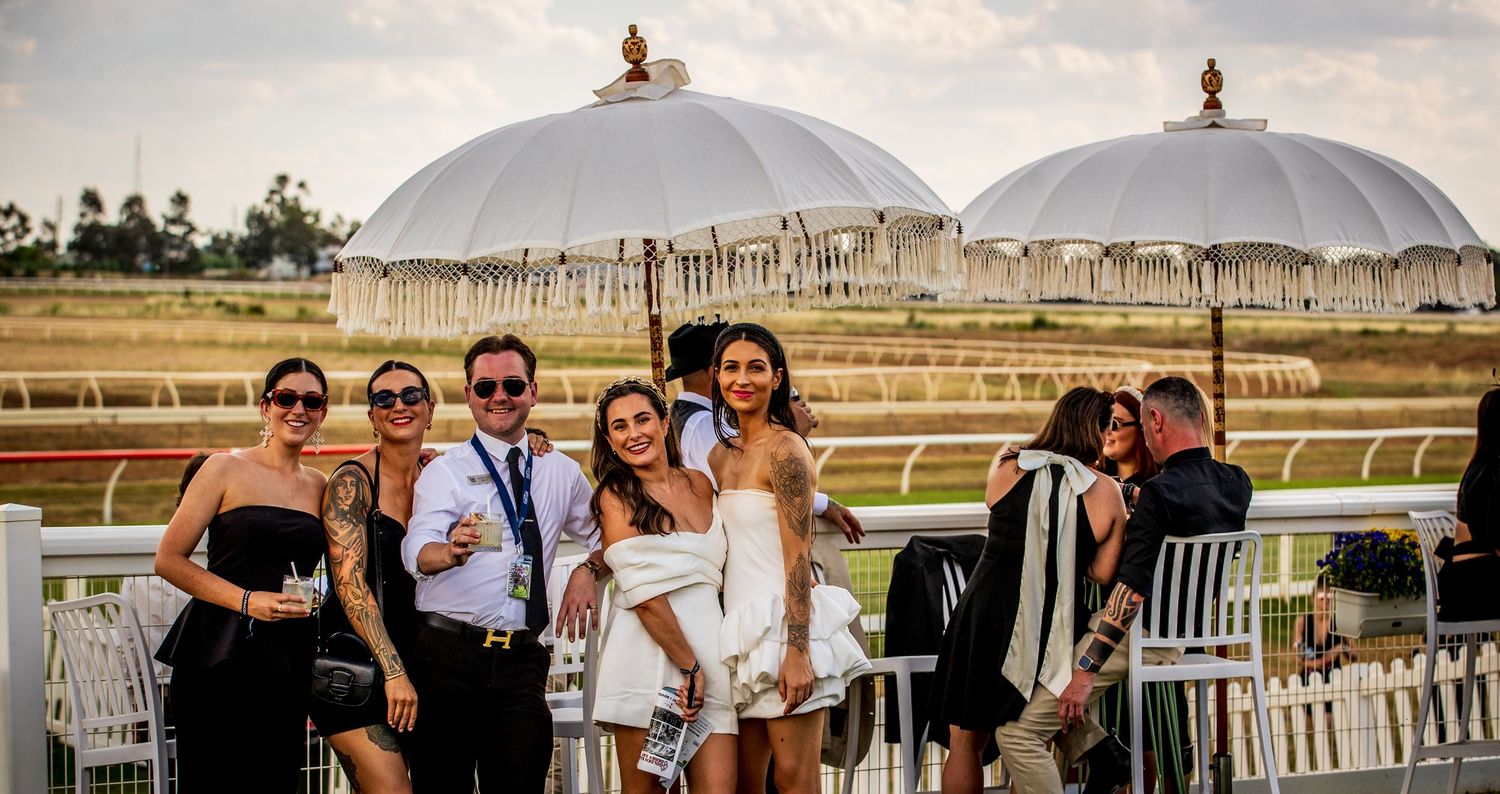A group of people celebrate at a racetrack venue with drinks and festivities during a sunny day.