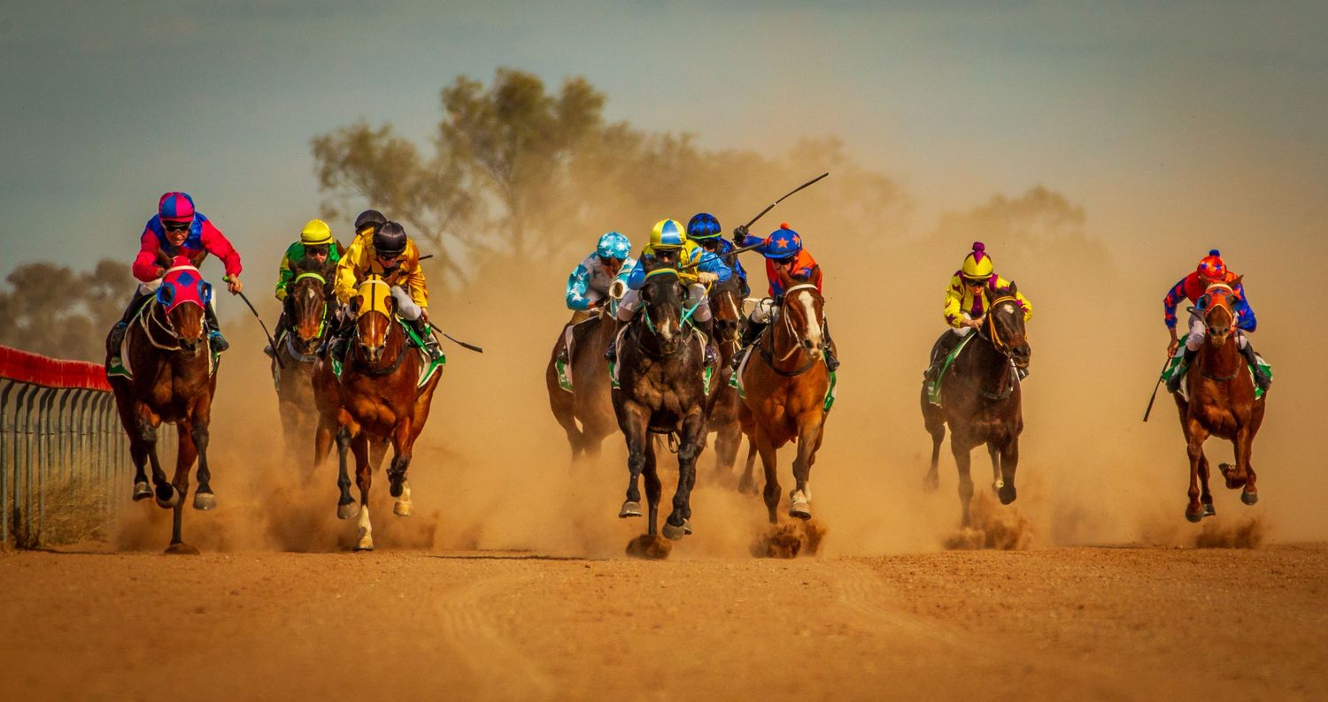 Jockeys on horseback racing across a dusty desert track in a colorful competitive horse race.