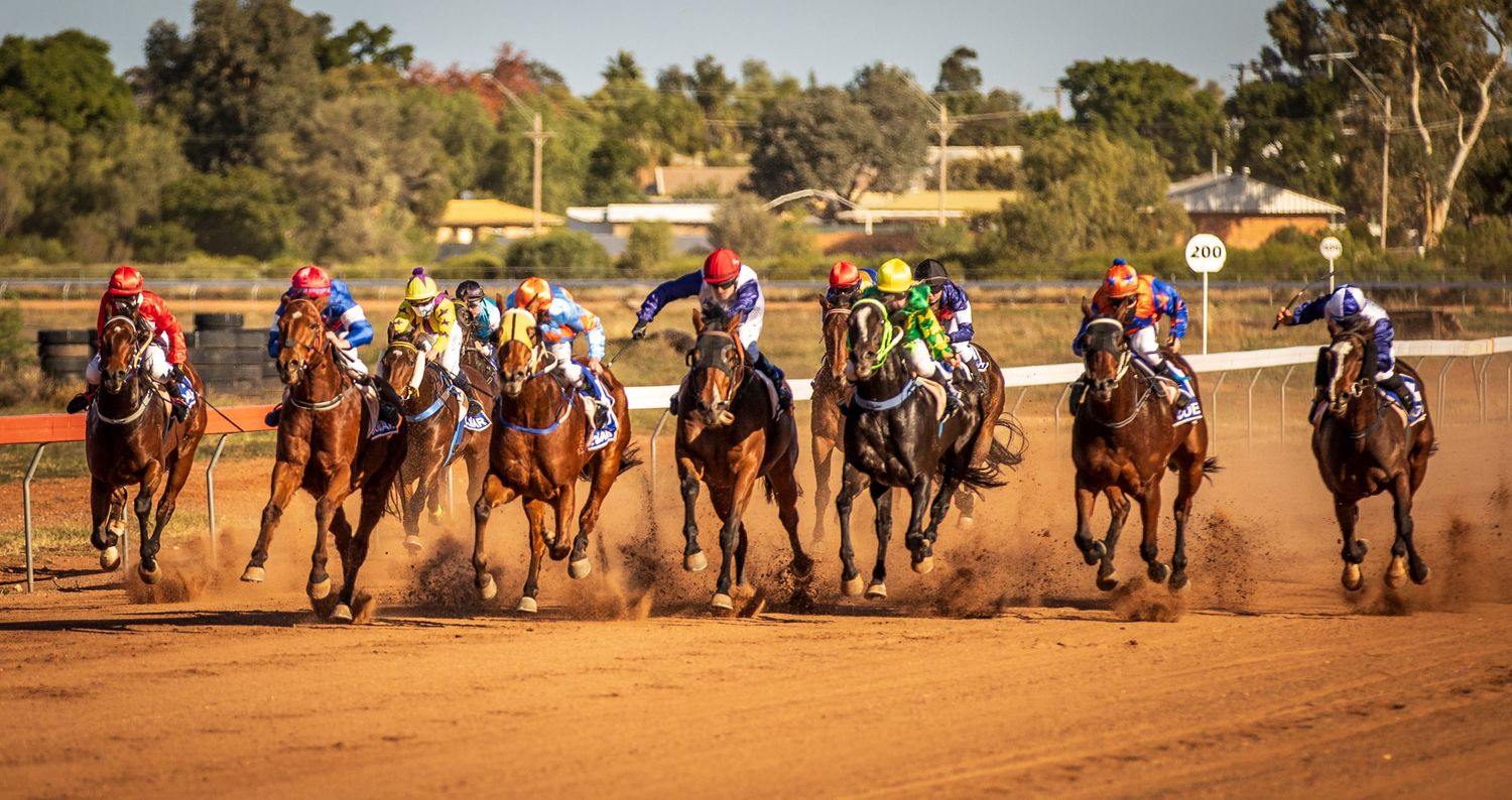 Horse racing sequence showing multiple horses and riders competing on a dusty track during a race event.