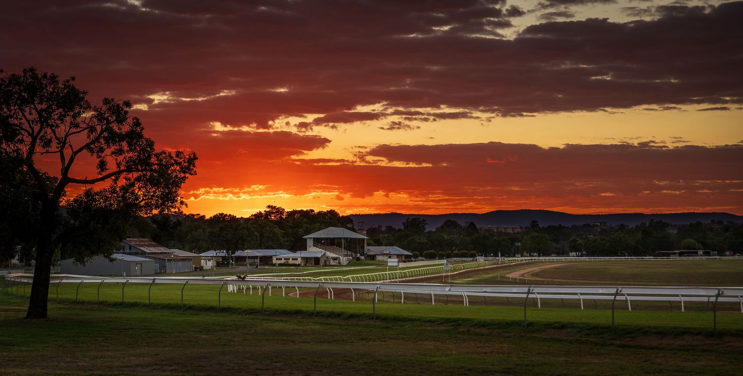 Stunning red and orange sunset over a rural racetrack with green fields and white fencing in Australia.