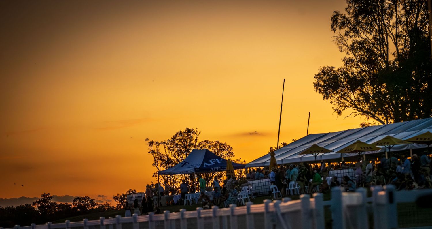 Stunning golden sunset silhouettes a crowded outdoor event with white tents and trees against a vibrant orange sky.