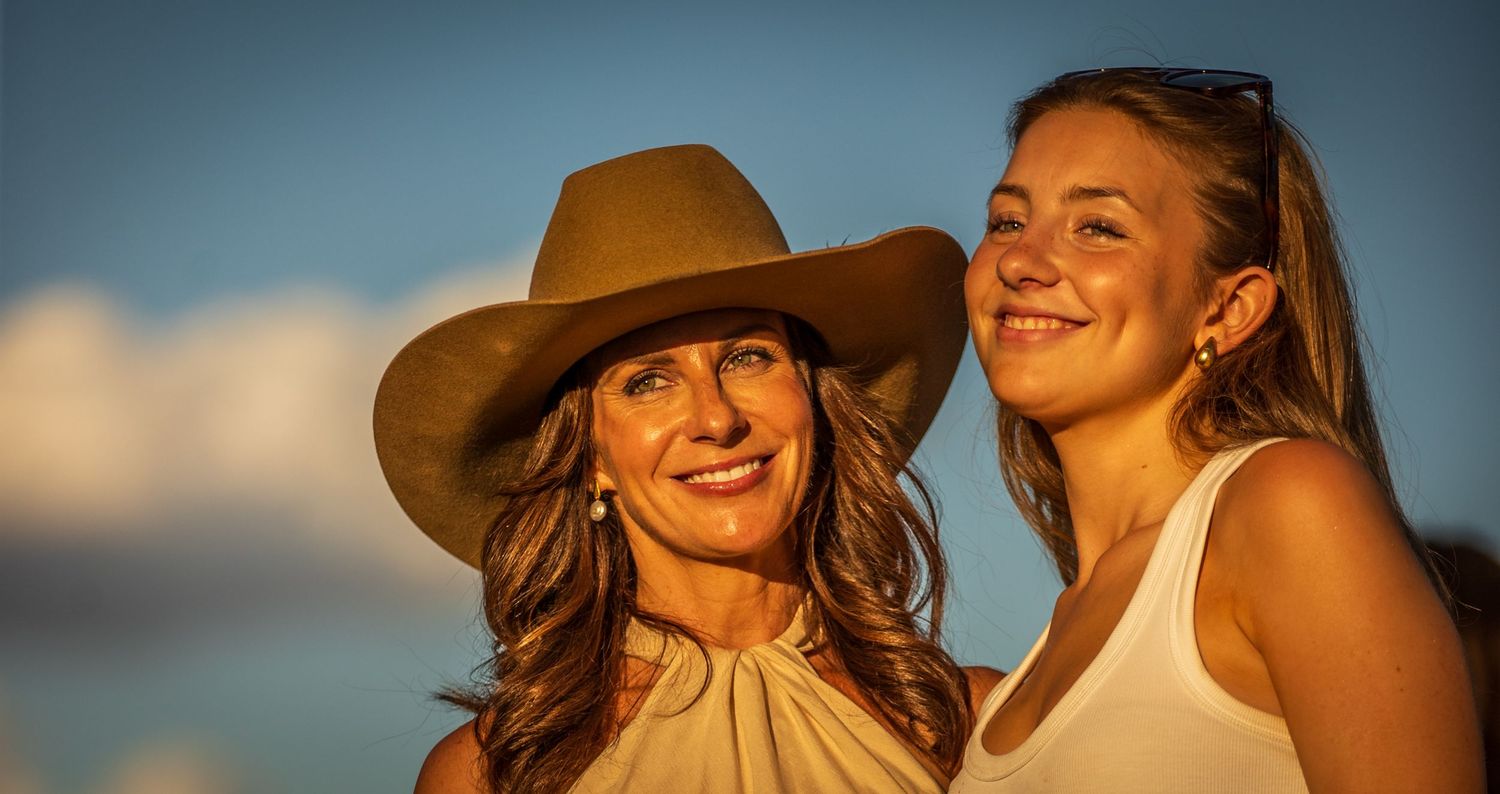 People enjoying a sunset together at the beach wearing casual summer attire and wide-brimmed hats.