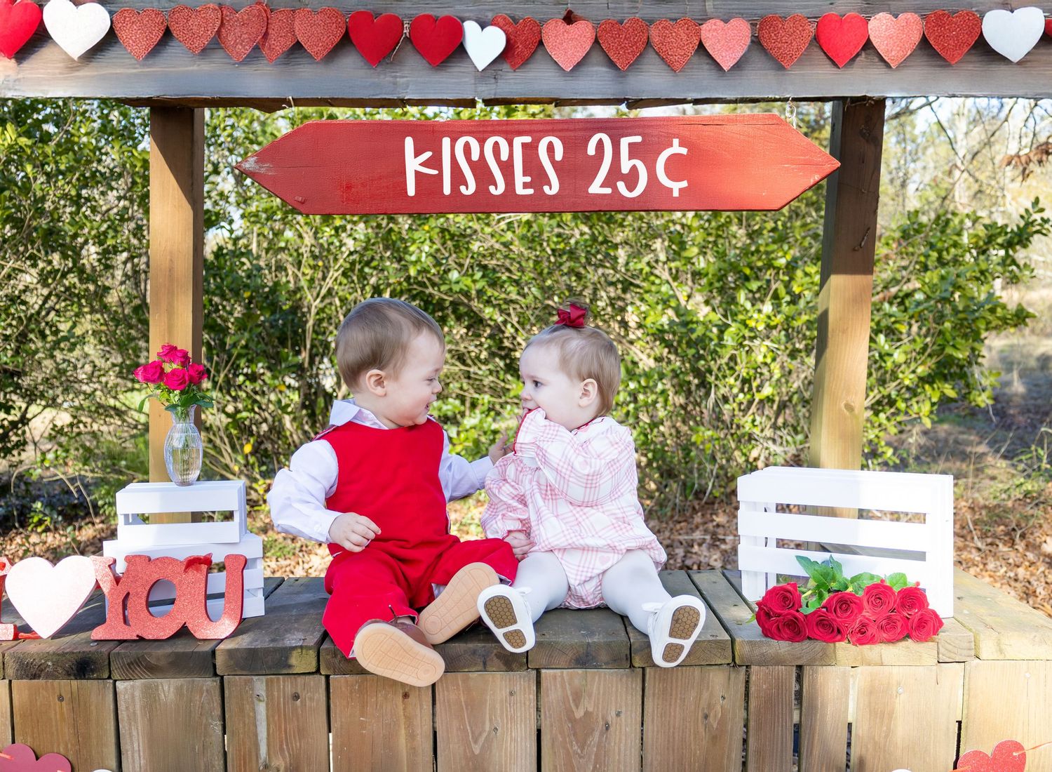 A wooden fence decorated with pink and red heart cutouts and a sign reading 'Kisses 25 cents' for Valentine's Day.