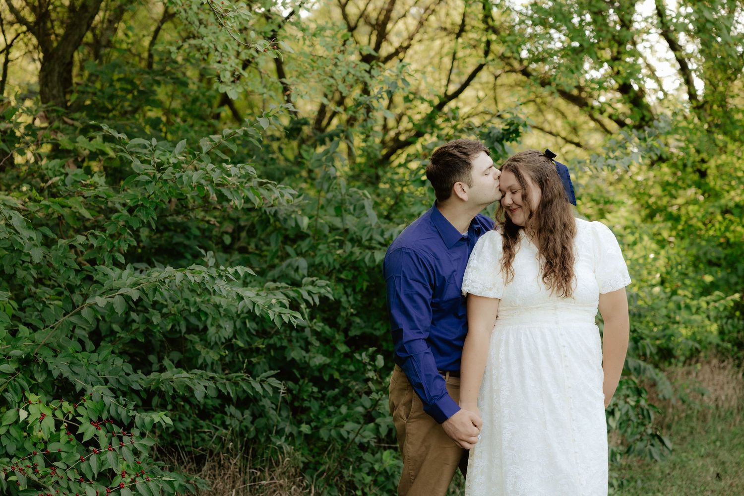 A couple walking hand in hand through lush green foliage on a summer afternoon.