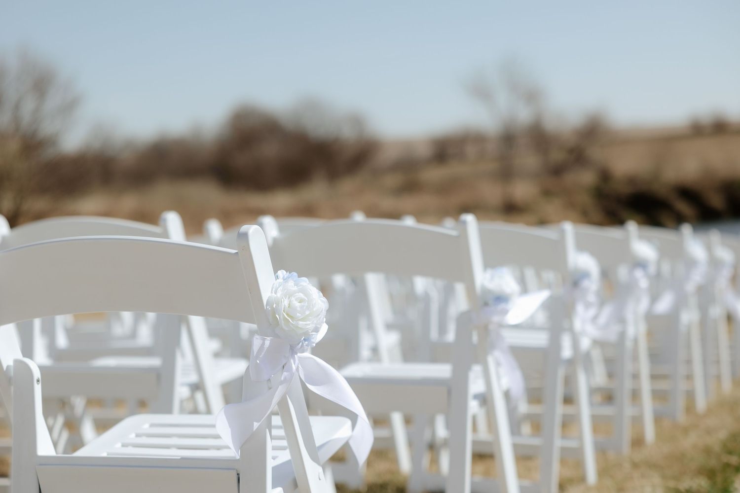 White folding chairs with elegant ribbon and rose decorations arranged in rows for an outdoor wedding ceremony at Sparks Barn