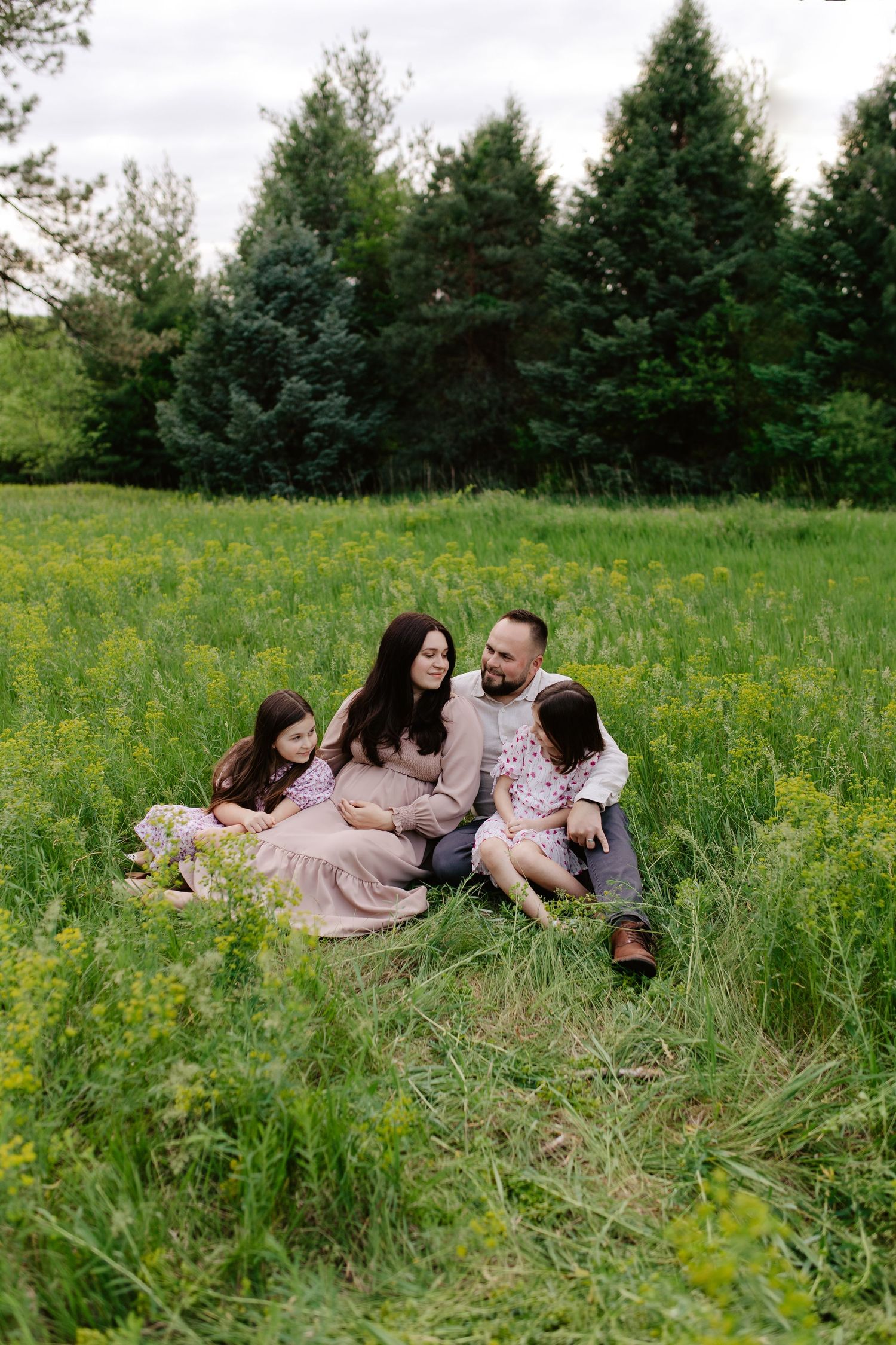 A family relaxes together in a sunny meadow filled with yellow wildflowers and tall grass.