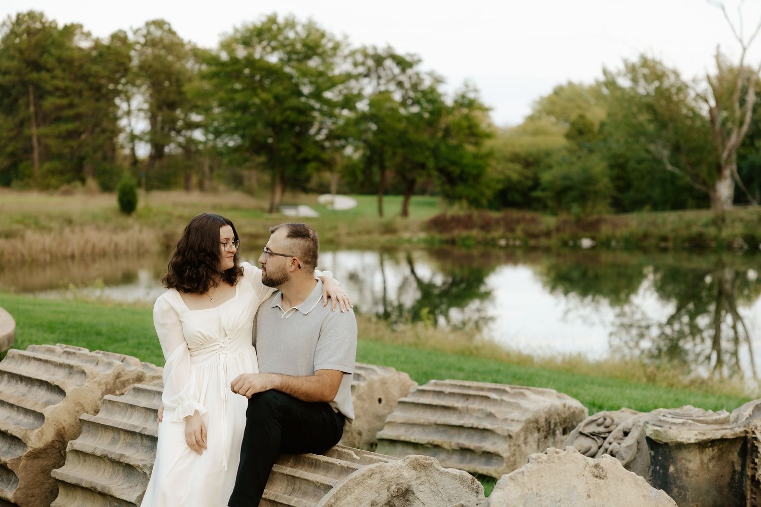 Couple shares romantic moment against stone pillars at sunset during outdoor wedding photoshoot.
