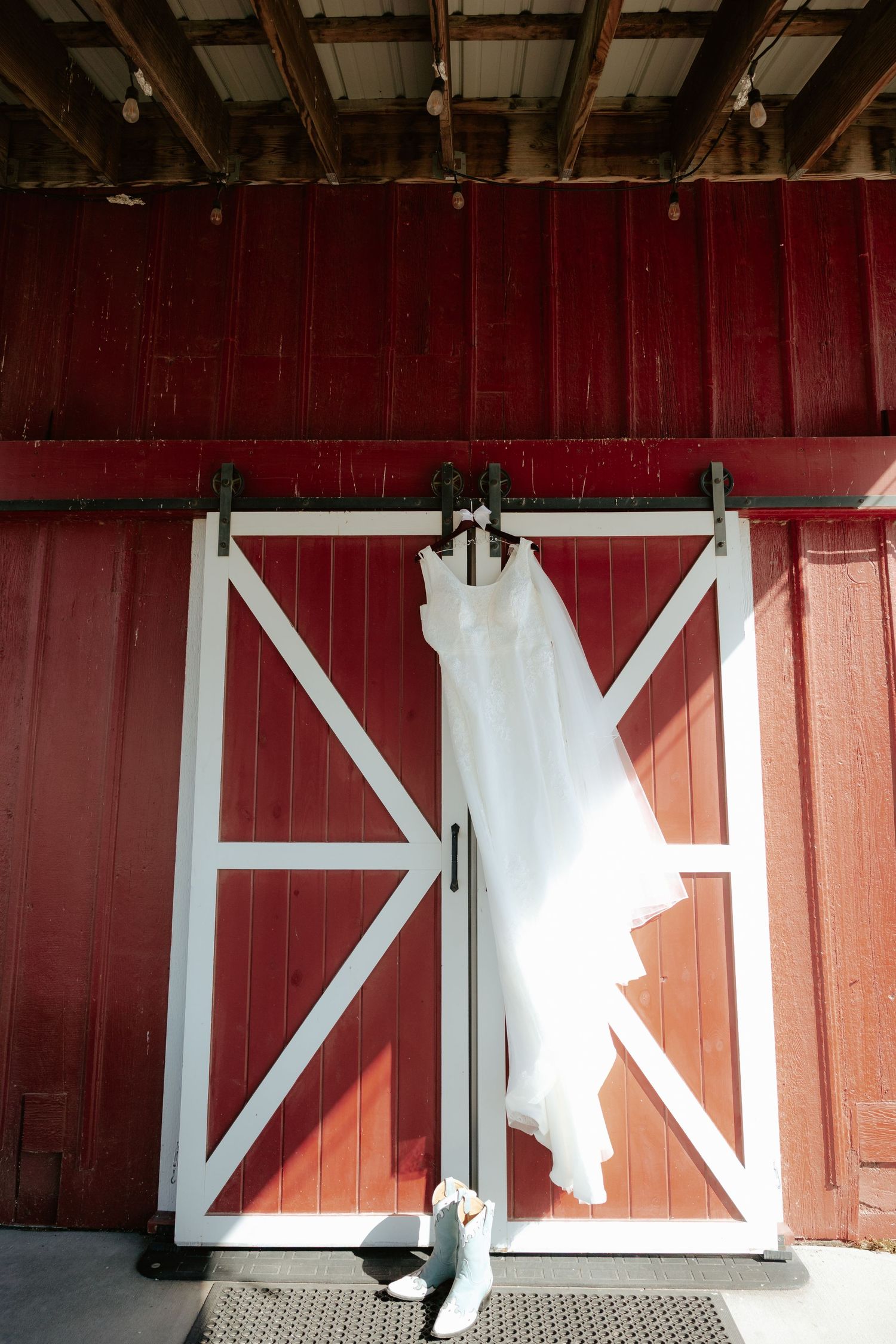 White wedding dress and bridal heels displayed against rustic red barn doors with white trim.