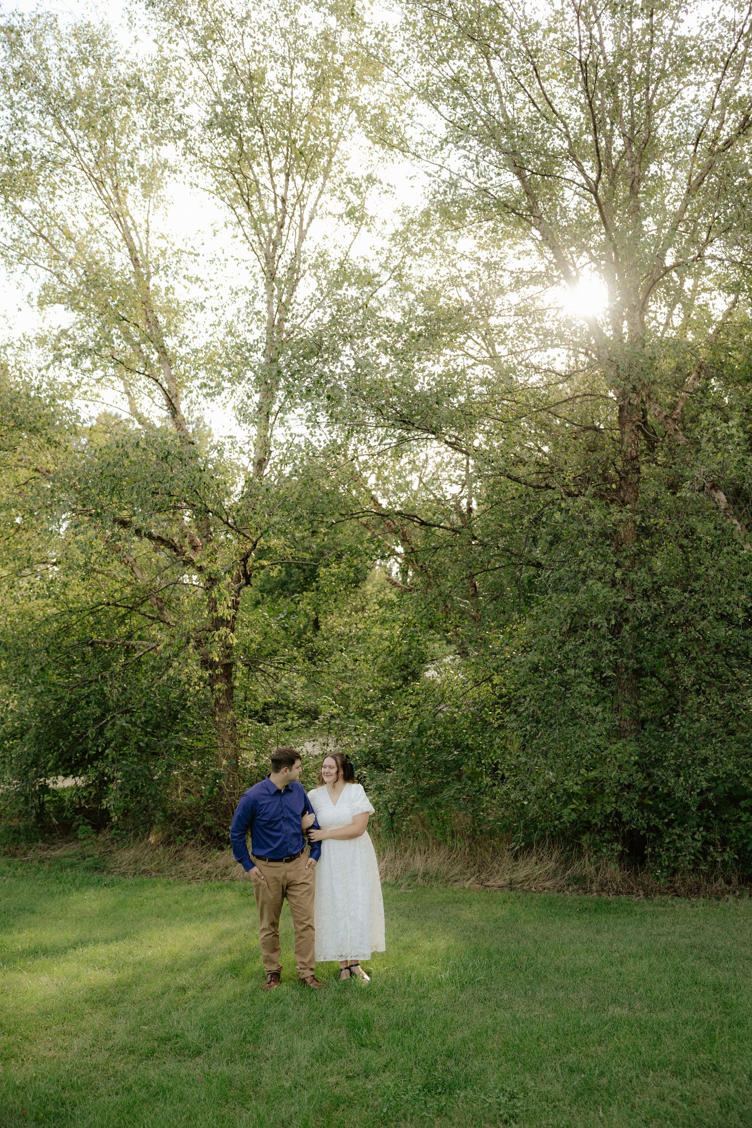 A couple walking hand in hand through lush green foliage on a summer afternoon.