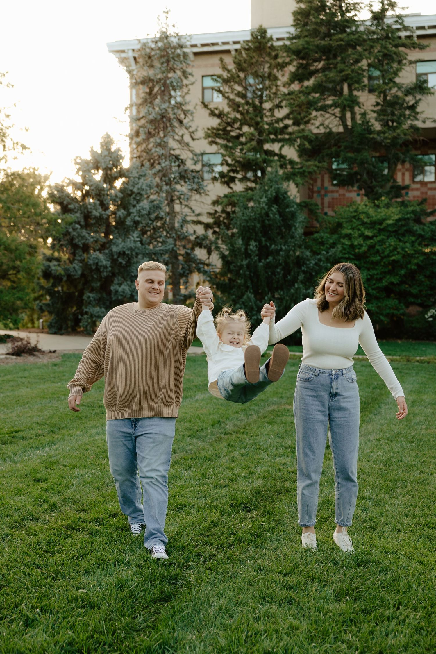 A couple swings their toddler during a sunset photoshoot in Lincoln, Nebraska.