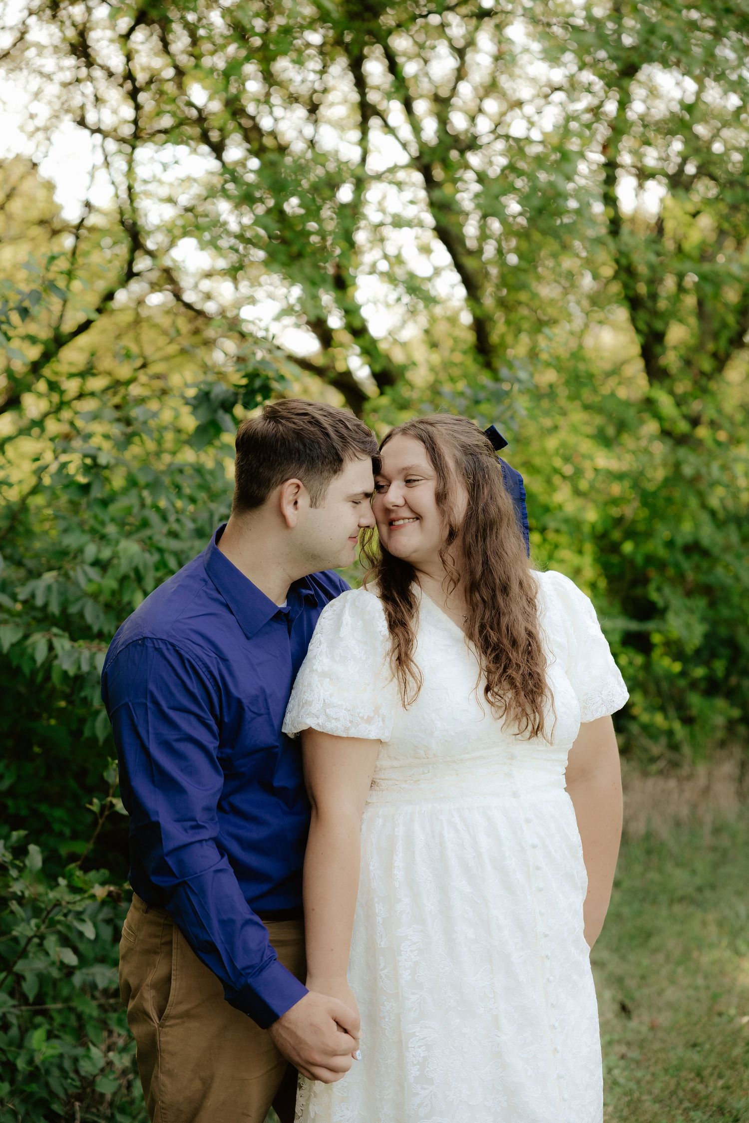 A couple walking hand in hand through lush green foliage on a summer afternoon.