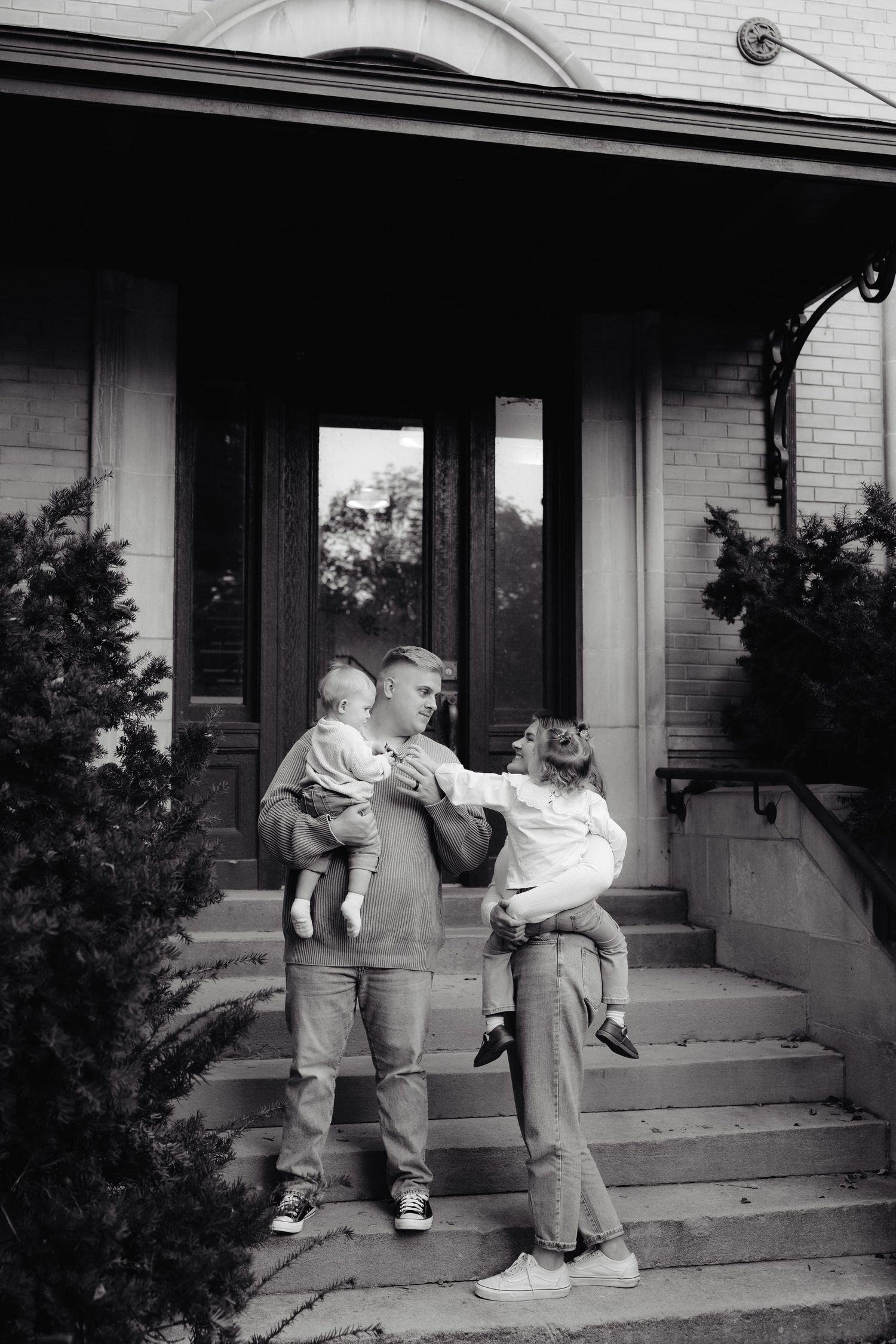 A sequence of black and white photos showing playful family interaction on front porch steps of a brick house.