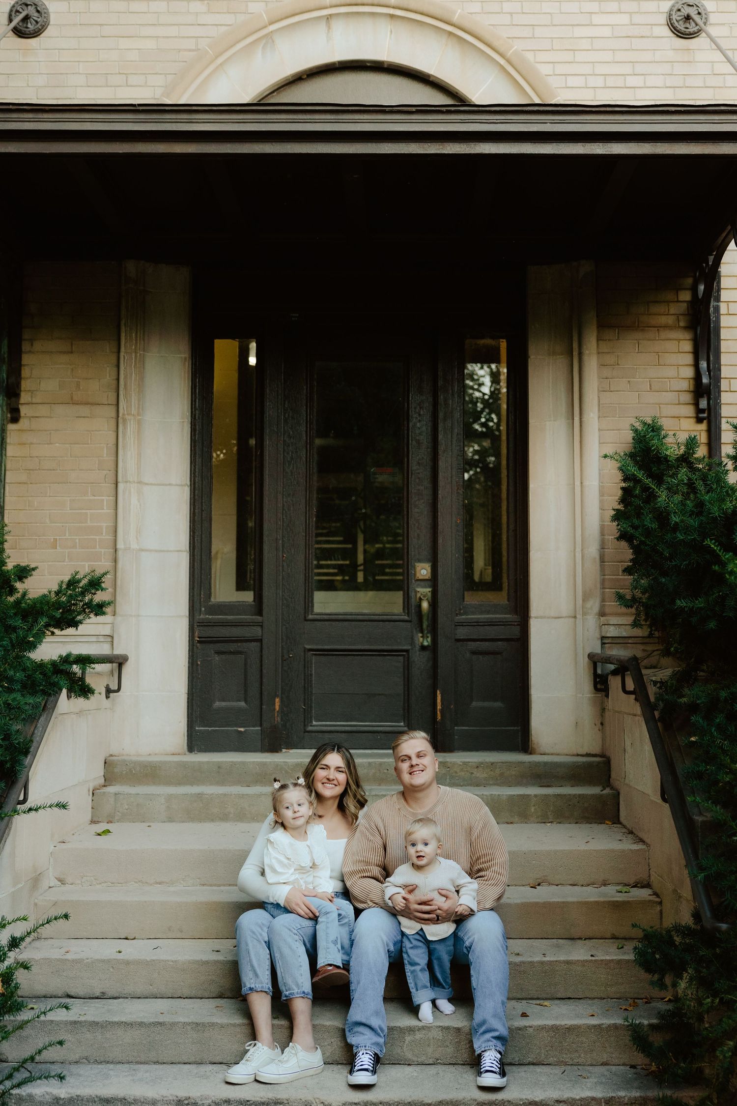 A family sits together on concrete steps outside a building during a family photo session.
