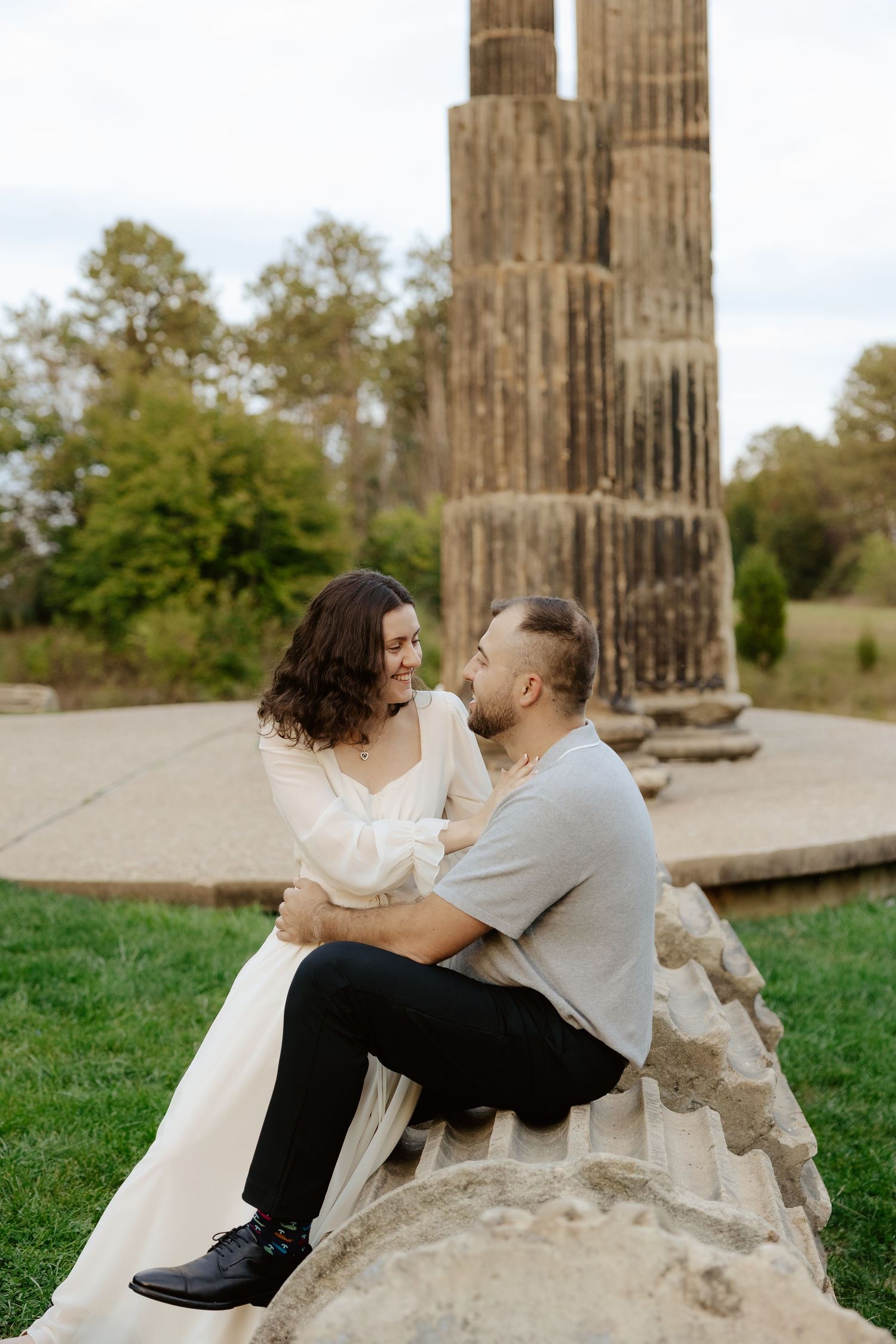 Couple shares romantic moment against stone pillars at sunset during outdoor wedding photoshoot.