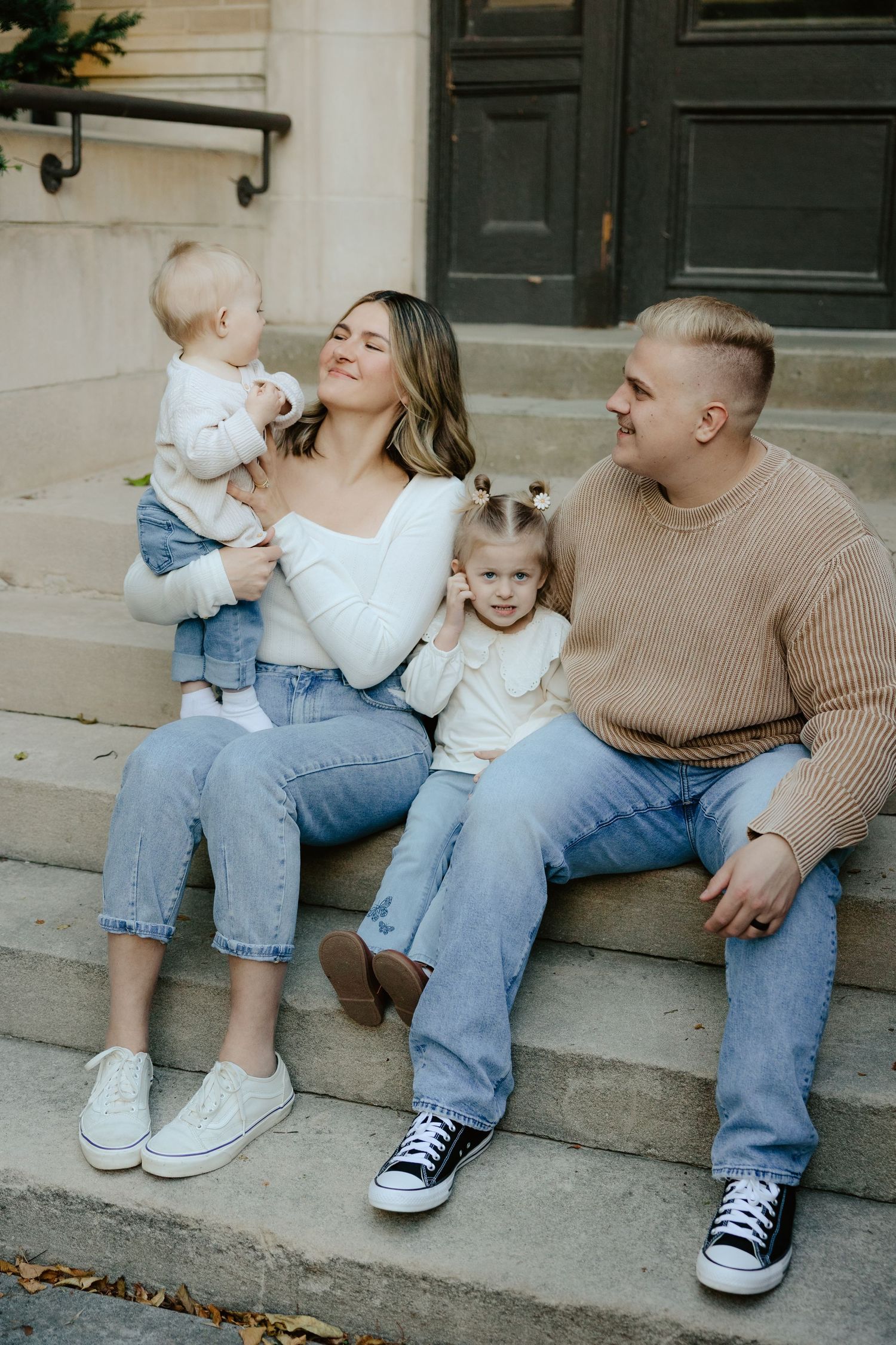 A family sits together on concrete steps outside a building during a family photo session.