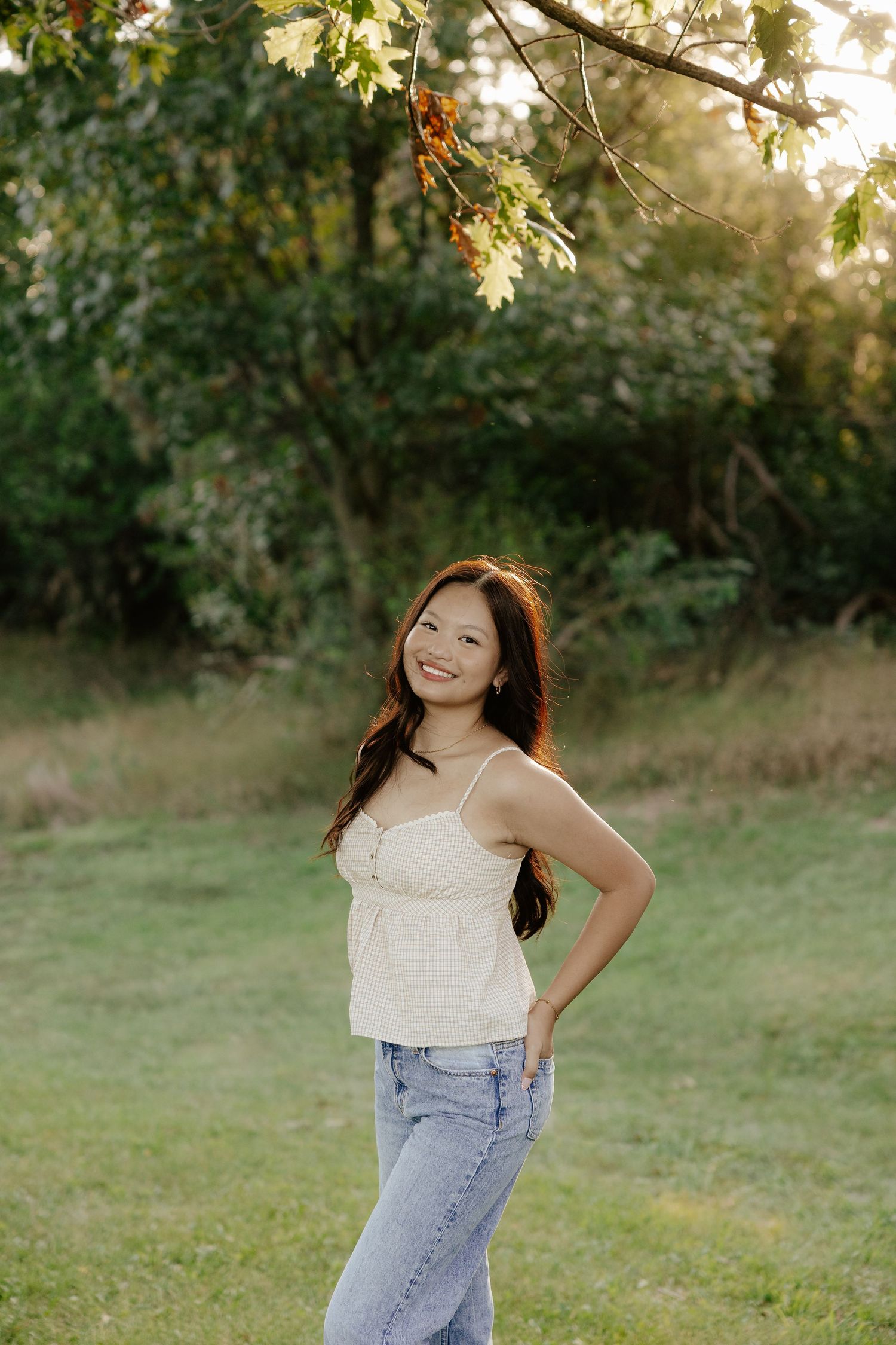 A girl walking through a grassy field in casual clothing at sunset for her senior photo session.