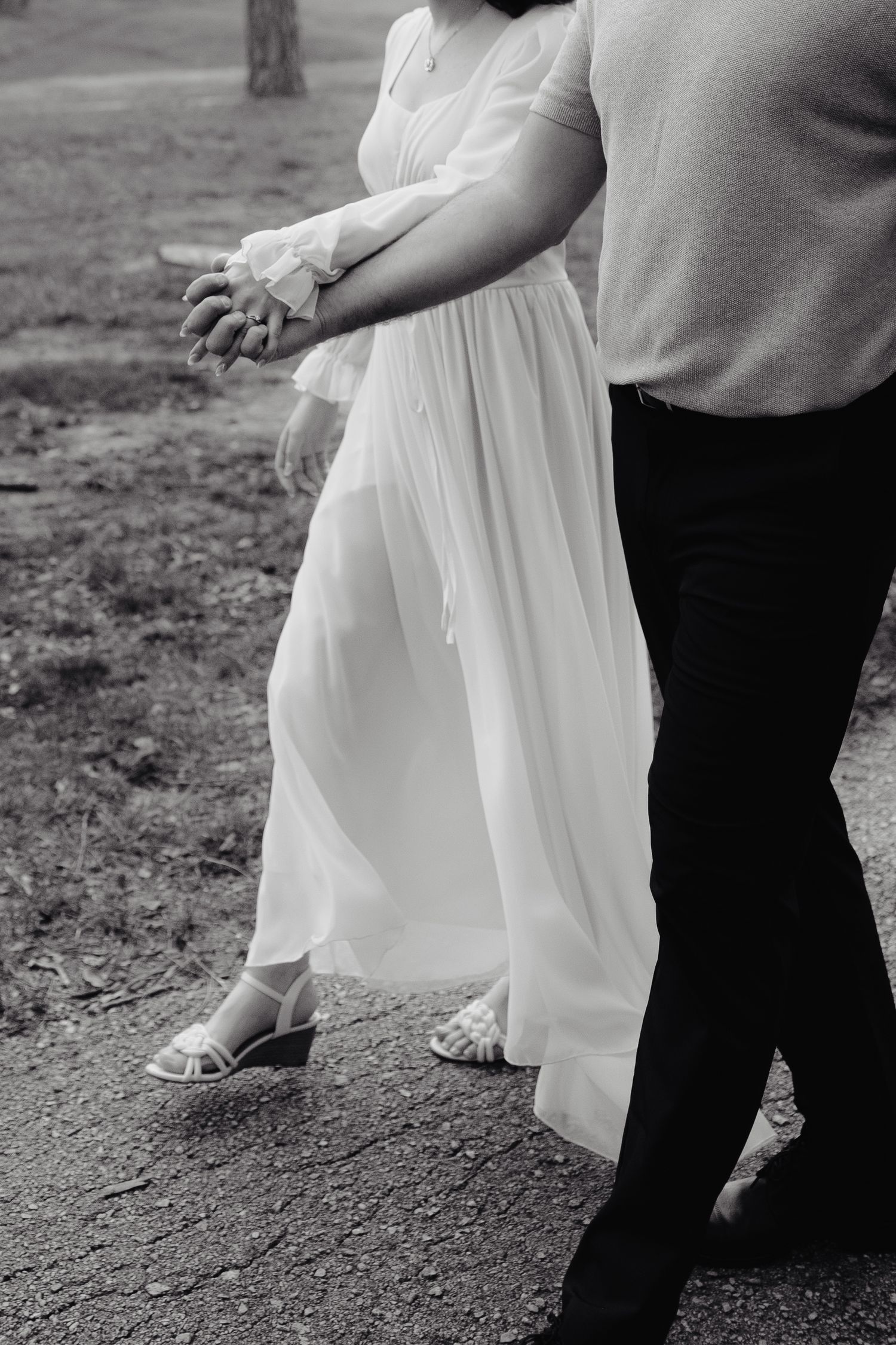 Black and white photo of a couple walking together on a tree-lined path in a romantic outdoor setting.