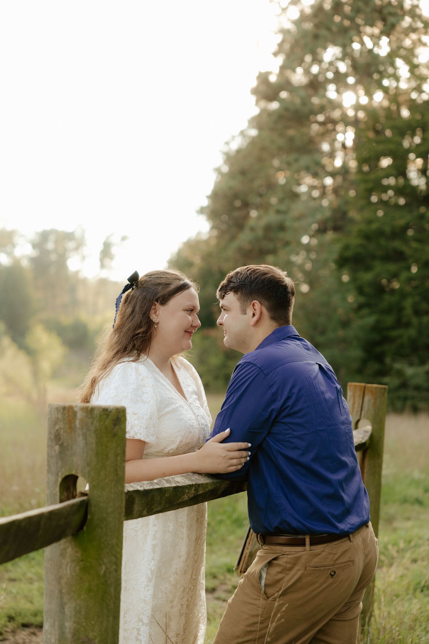 A couple embraces tenderly in an outdoor setting while wearing blue and white outfits in golden sunlight.