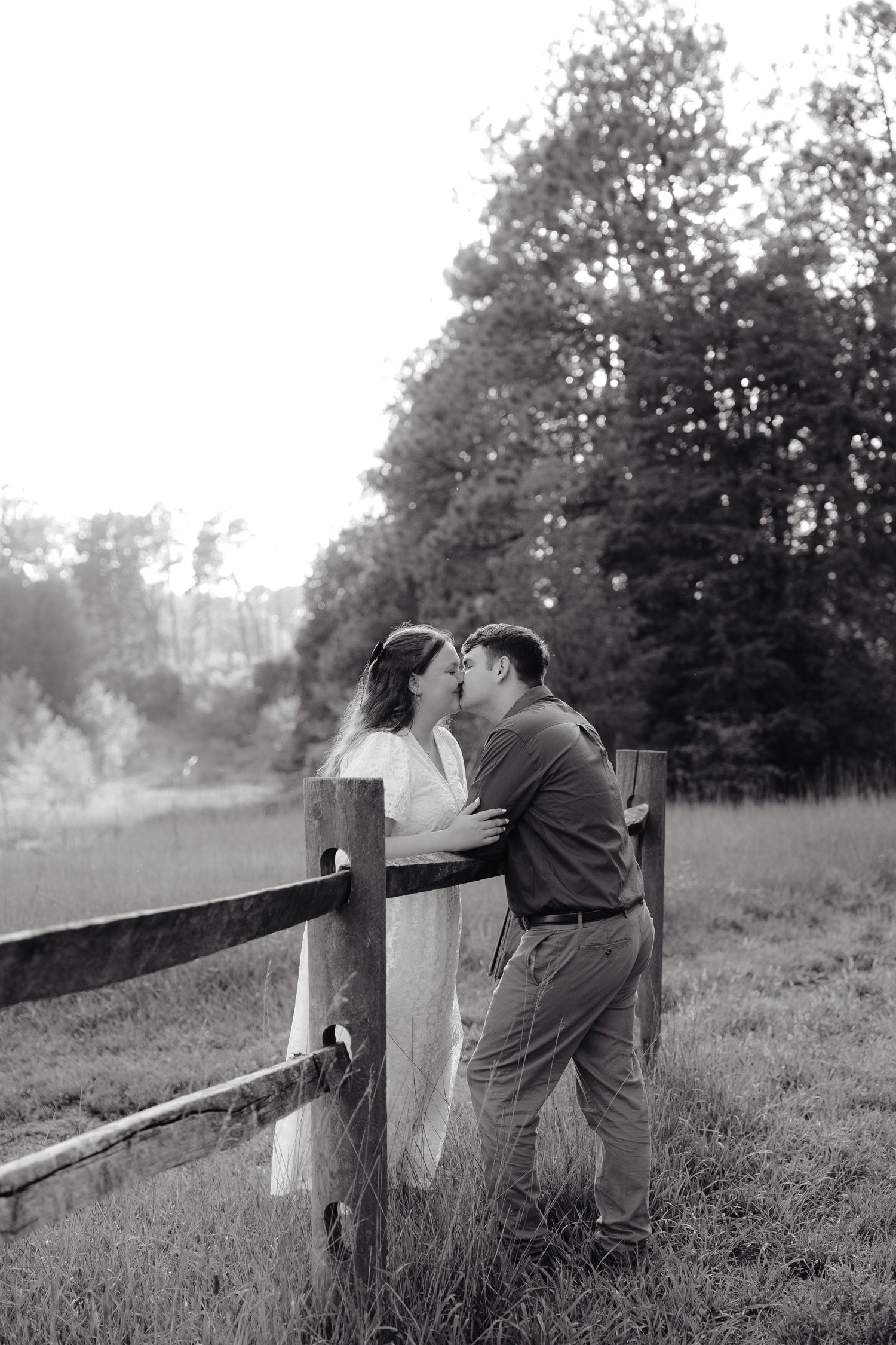 A couple embraces tenderly in an outdoor setting while wearing blue and white outfits in golden sunlight.