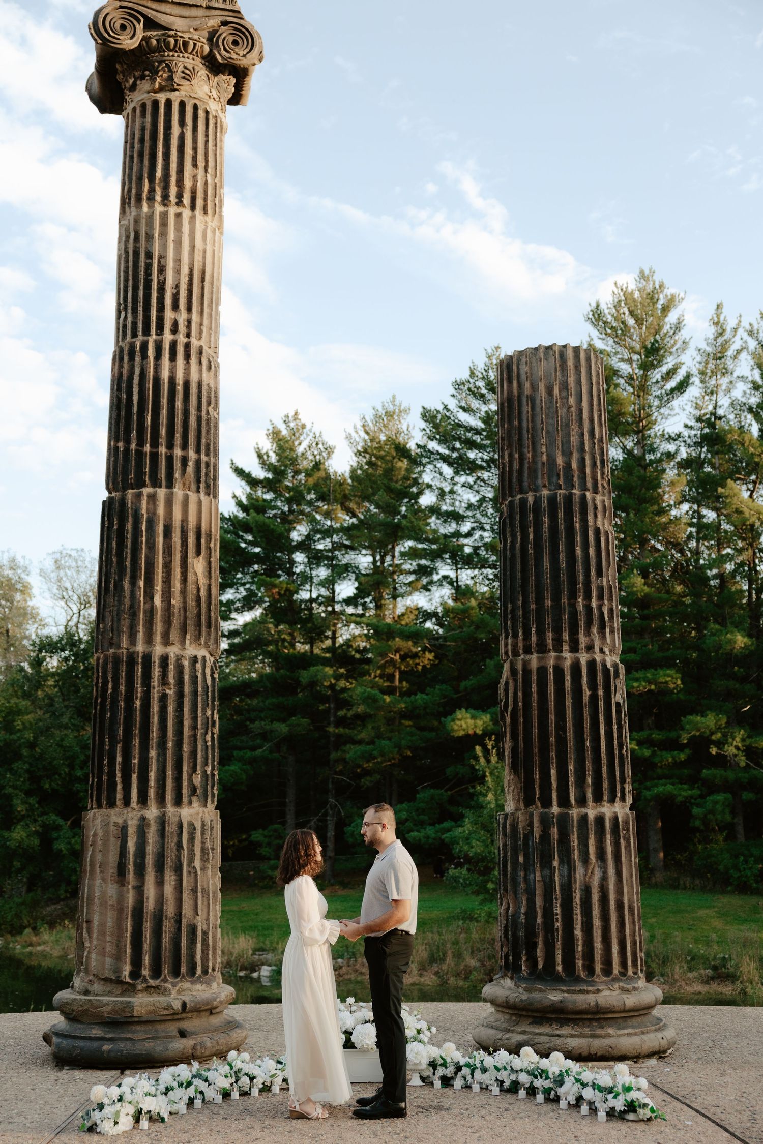 Couple shares romantic moment against stone pillars at sunset during outdoor wedding photoshoot.