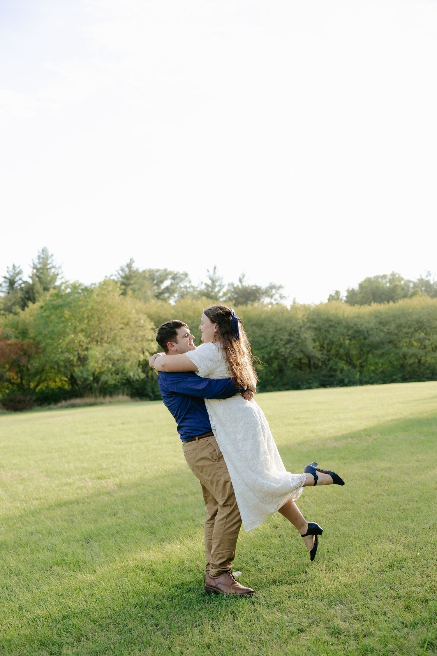 A couple engage in playful interaction across a grassy hillside during a warm sunset  engagement photoshoot.