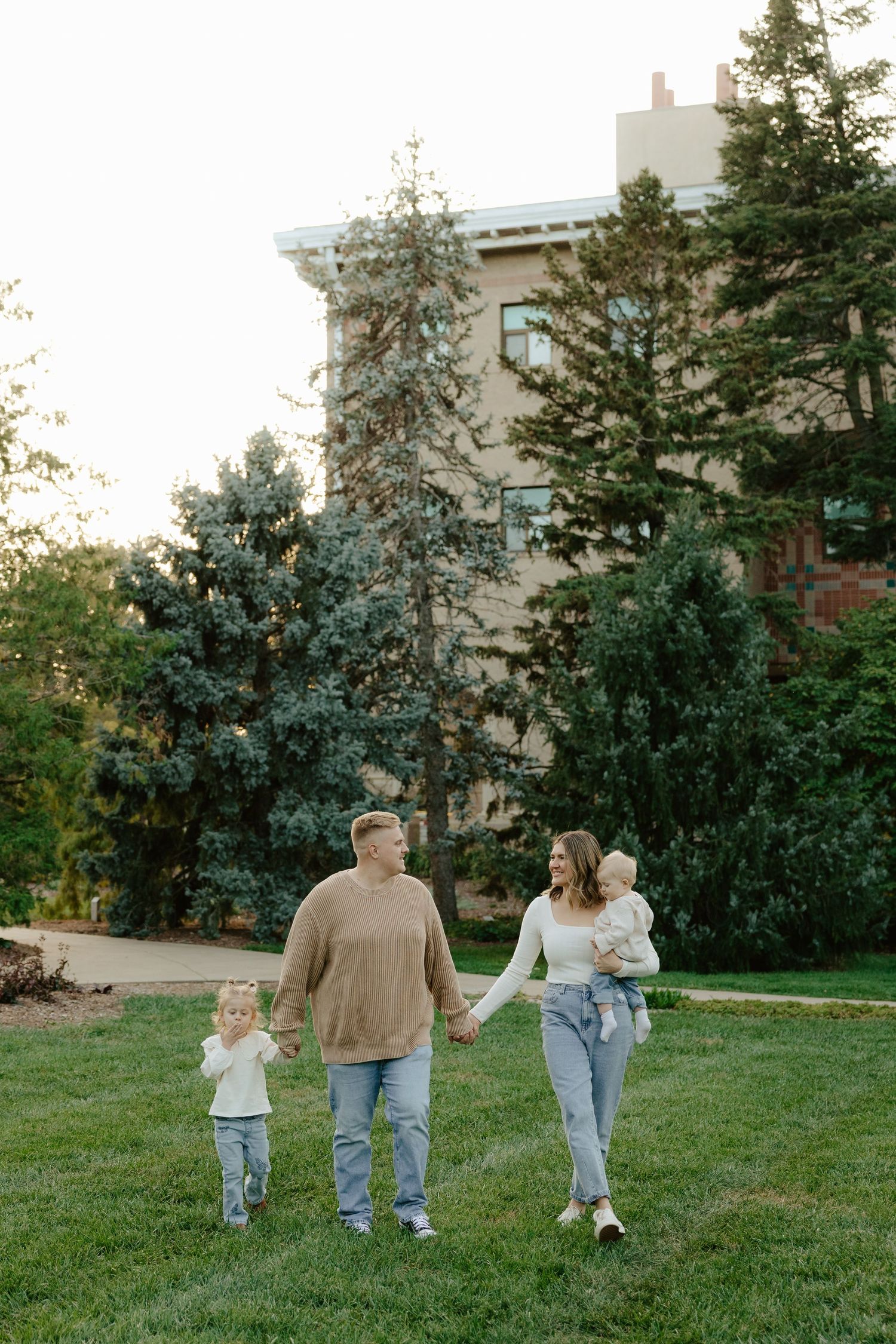 A family walks together holding hands across a green lawn with buildings visible in the background.