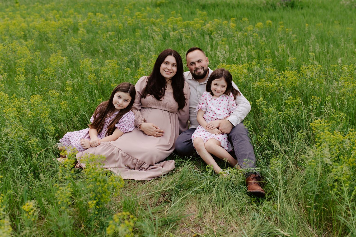 A family sits together on a in a lush green meadow filled with wildflowers on a sunny day.