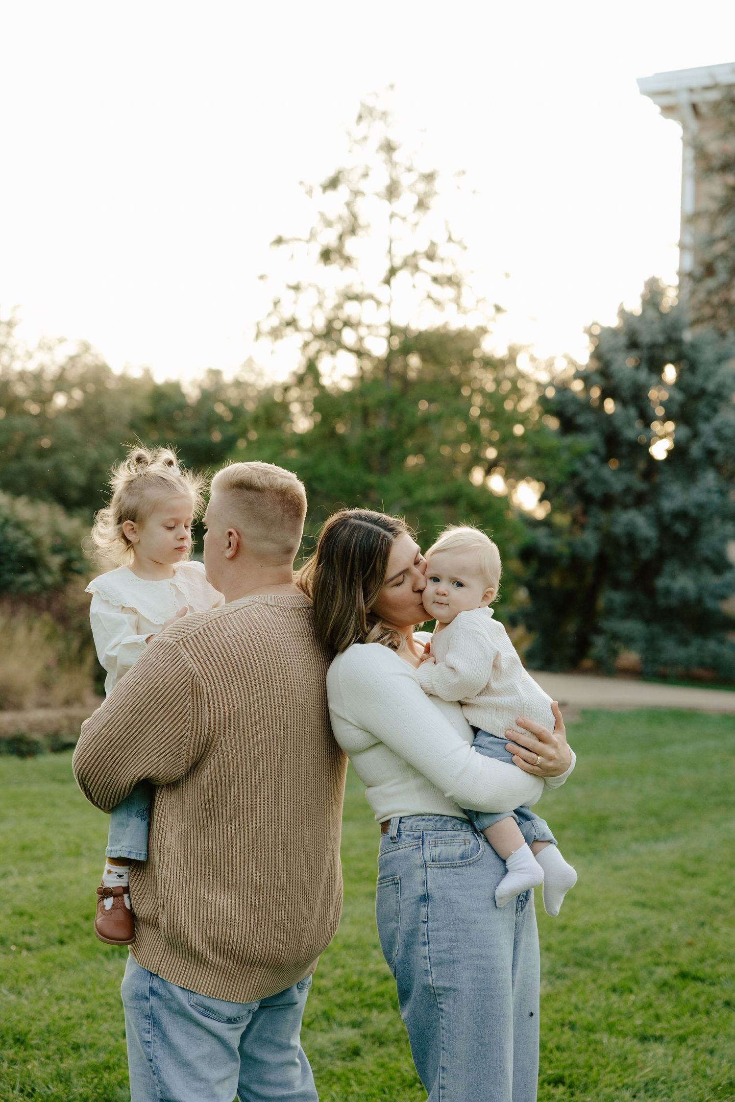A family shares tender moments together while standing on a grassy lawn during golden hour.