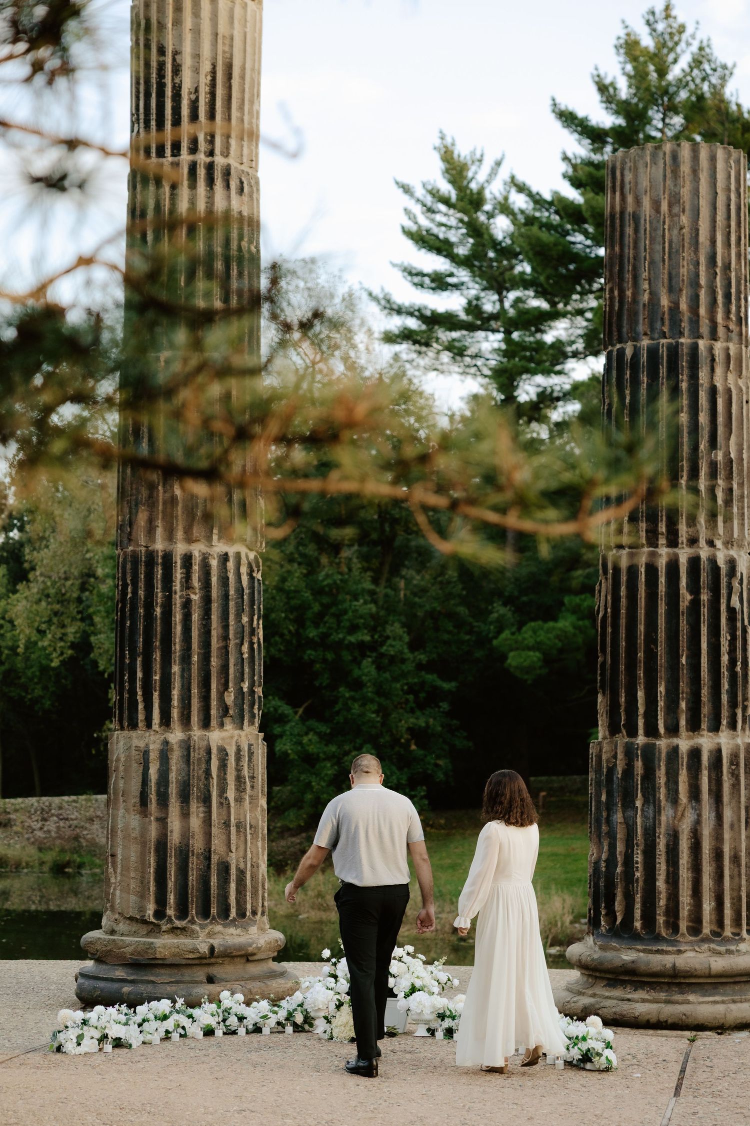 Couple shares romantic moment against stone pillars at sunset during outdoor wedding photoshoot.