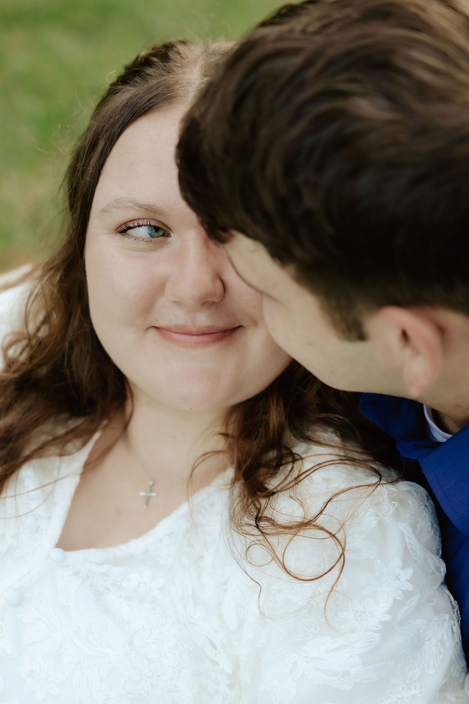 A couple sits together on grass in a natural outdoor setting surrounded by green trees and foliage at Pioneers Park in Lincoln Nebraska.