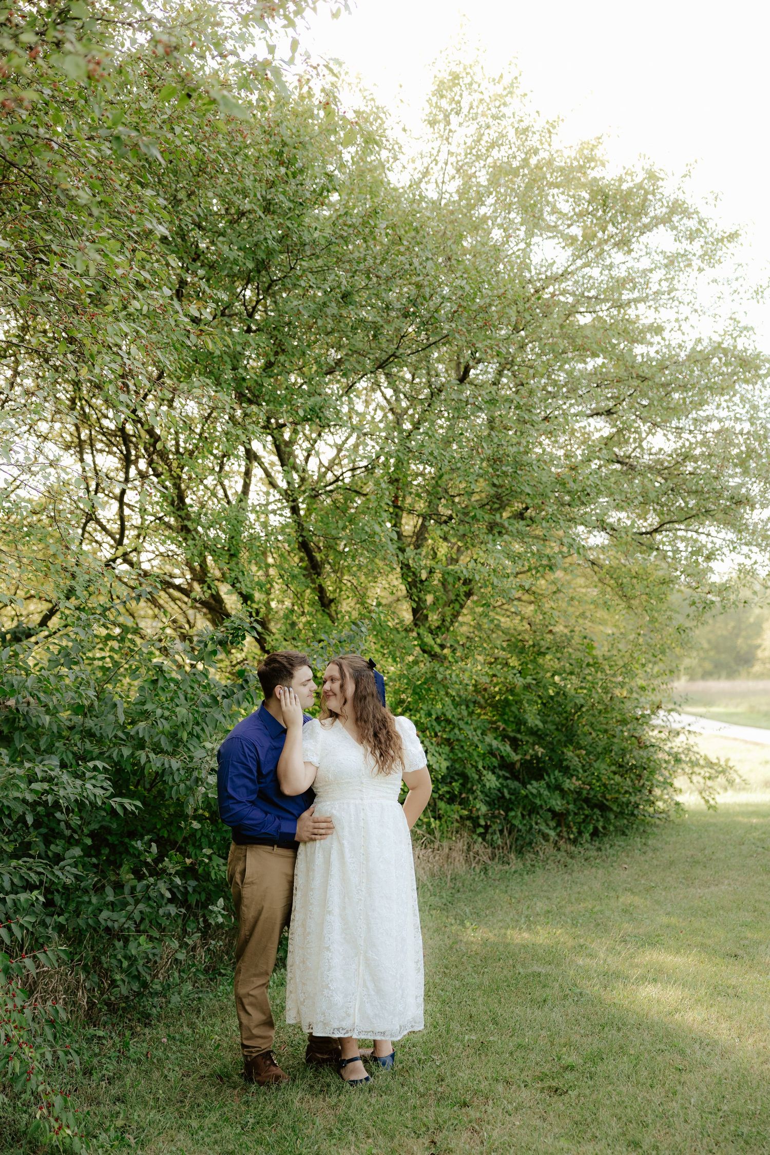 A couple walking hand in hand through lush green foliage on a summer afternoon.