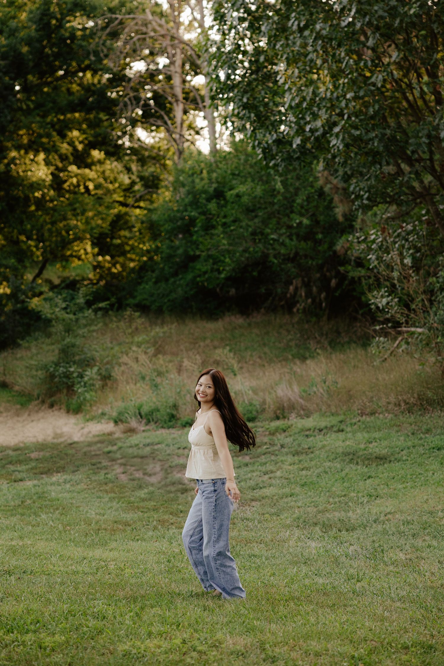 A girl walking through a grassy field in casual clothing at sunset for her senior photo session.