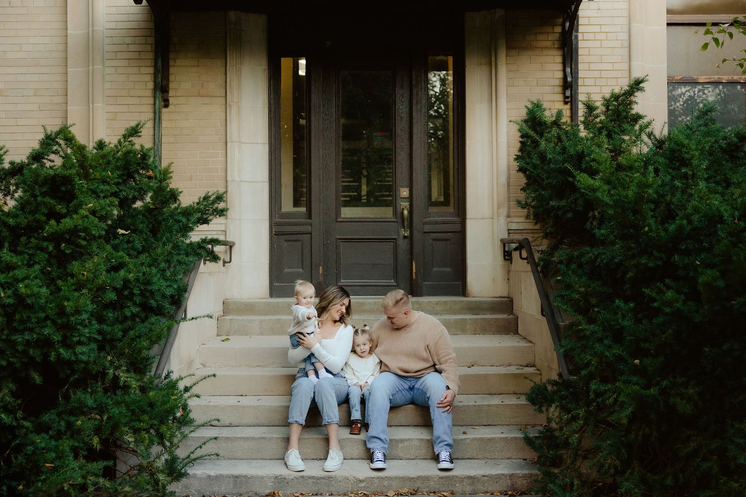 A family sits together on concrete steps outside a building during a family photo session.