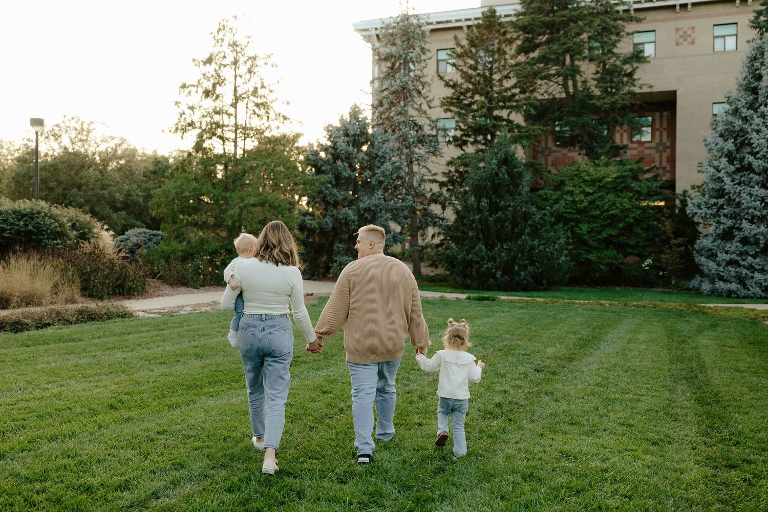 A family walks together holding hands across a green lawn with buildings visible in the background.